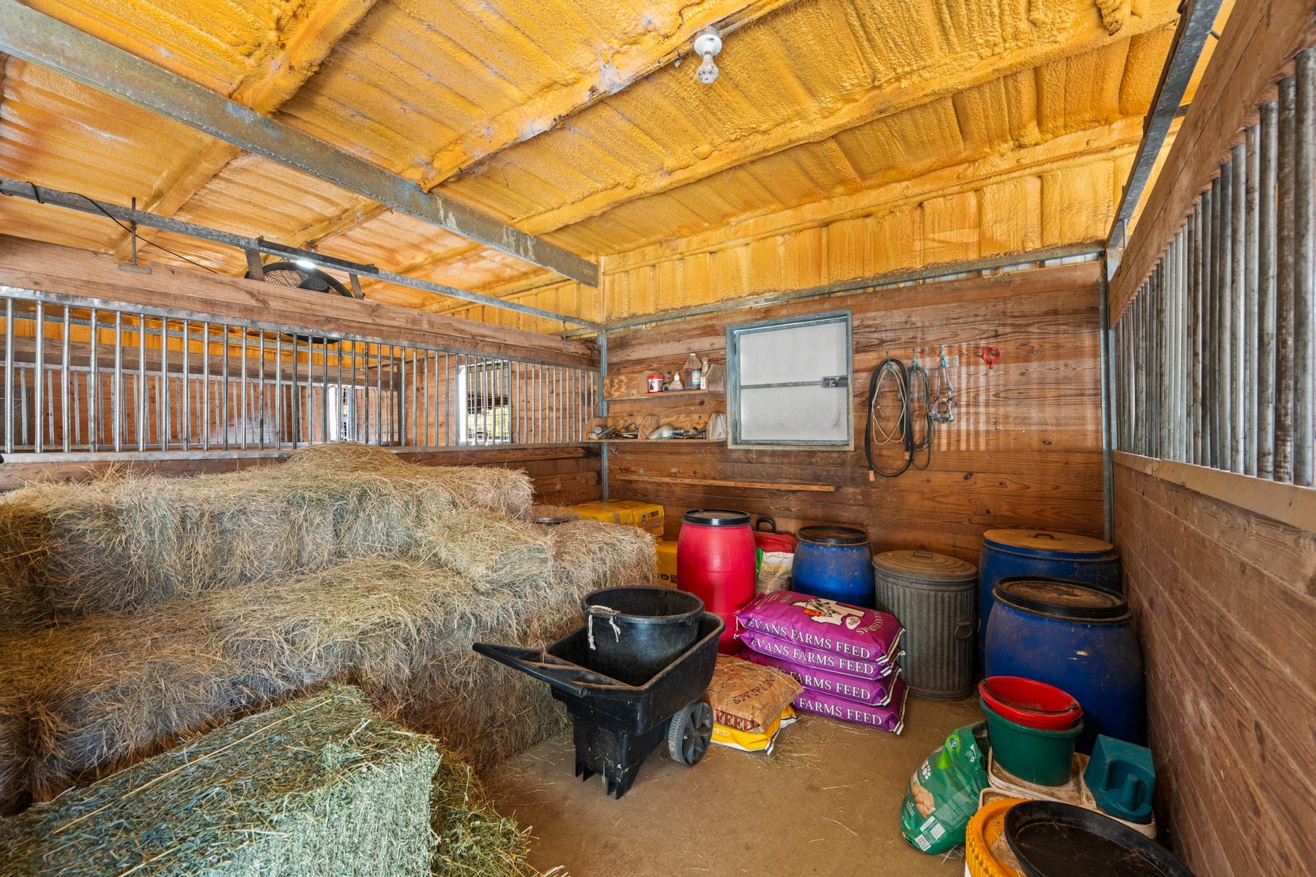 2215 Avenue Q, Santa Fe, TX 77510 Dedicated feed and hay storage room/extra stall offers space for hay bales, feed supplies, and tack essentials, with wood-paneled walls, metal-bar partitions, and overhead insulation.