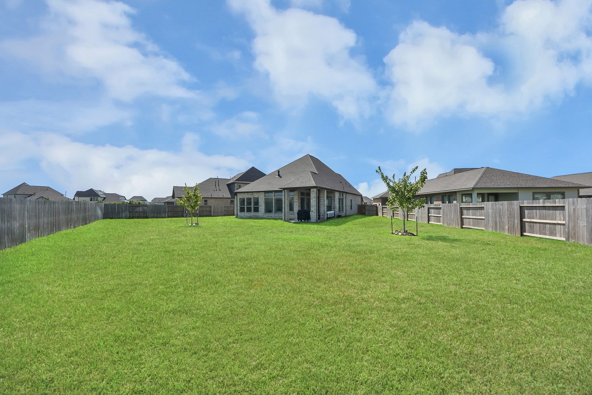 2995 Tantara Drive, Katy, TX 77493 Expansive backyard with lush green lawn and young trees, perfect for outdoor activities and relaxation, enclosed by a secure wooden fence.