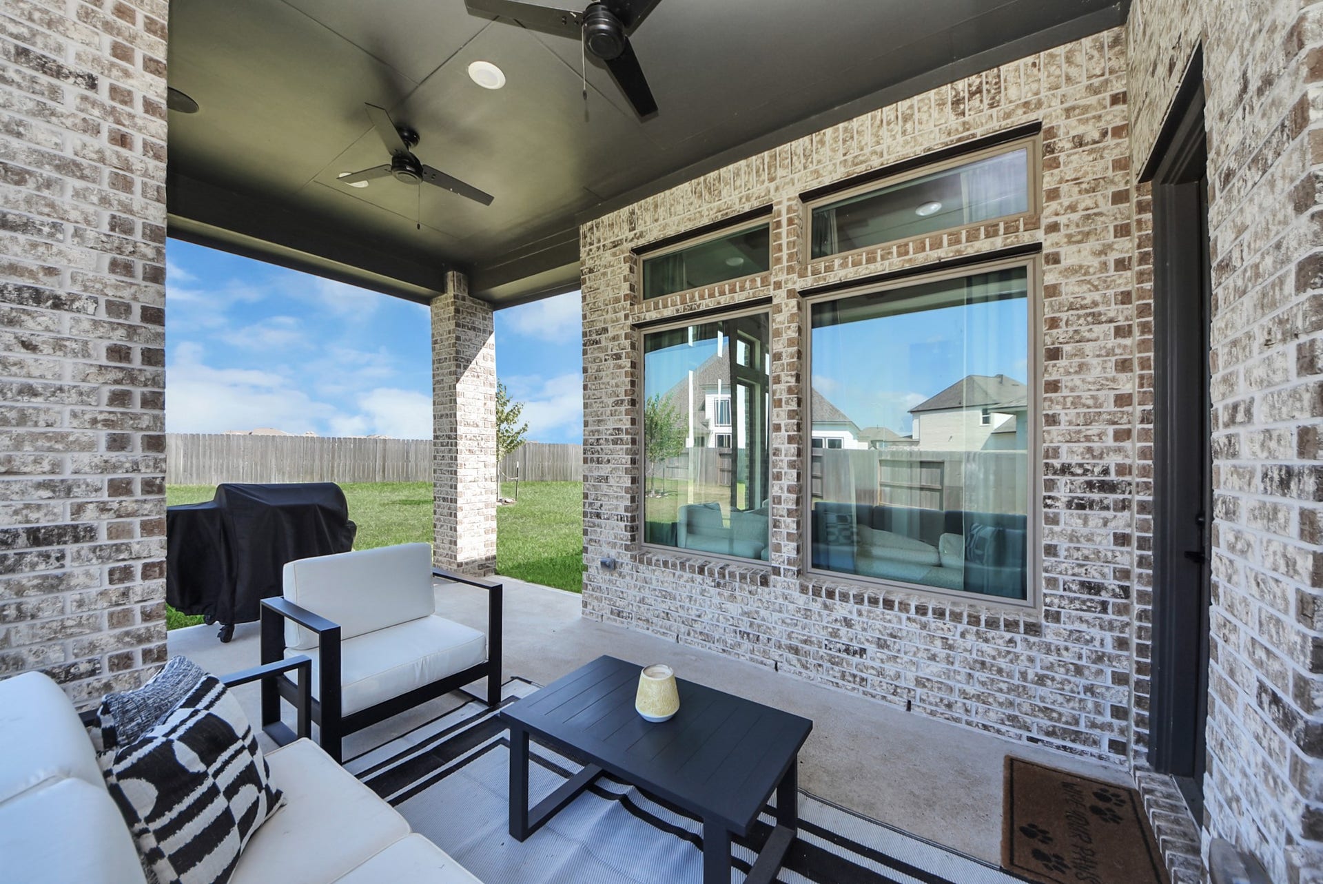 2995 Tantara Drive, Katy, TX 77493 Charming covered patio with stylish brickwork, perfect for outdoor relaxation, featuring cozy seating, a ceiling fan, and a view of the spacious backyard.