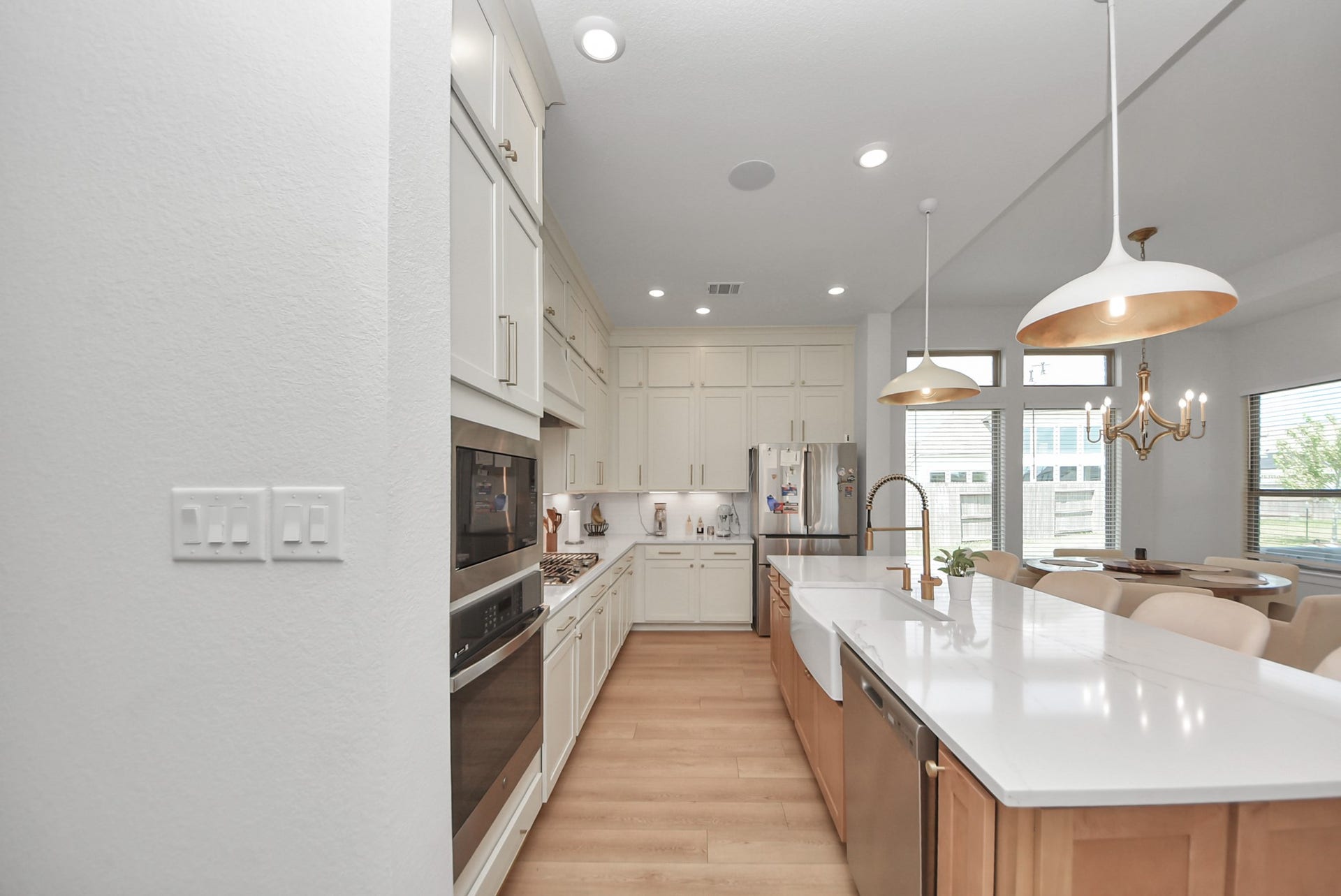 2995 Tantara Drive, Katy, TX 77493 Elegant kitchen featuring sleek white cabinetry, modern appliances, and a spacious island with a farmhouse sink. Bright pendant lighting complements the open-concept dining area with large windows, offering a warm and inviting atmosphere.