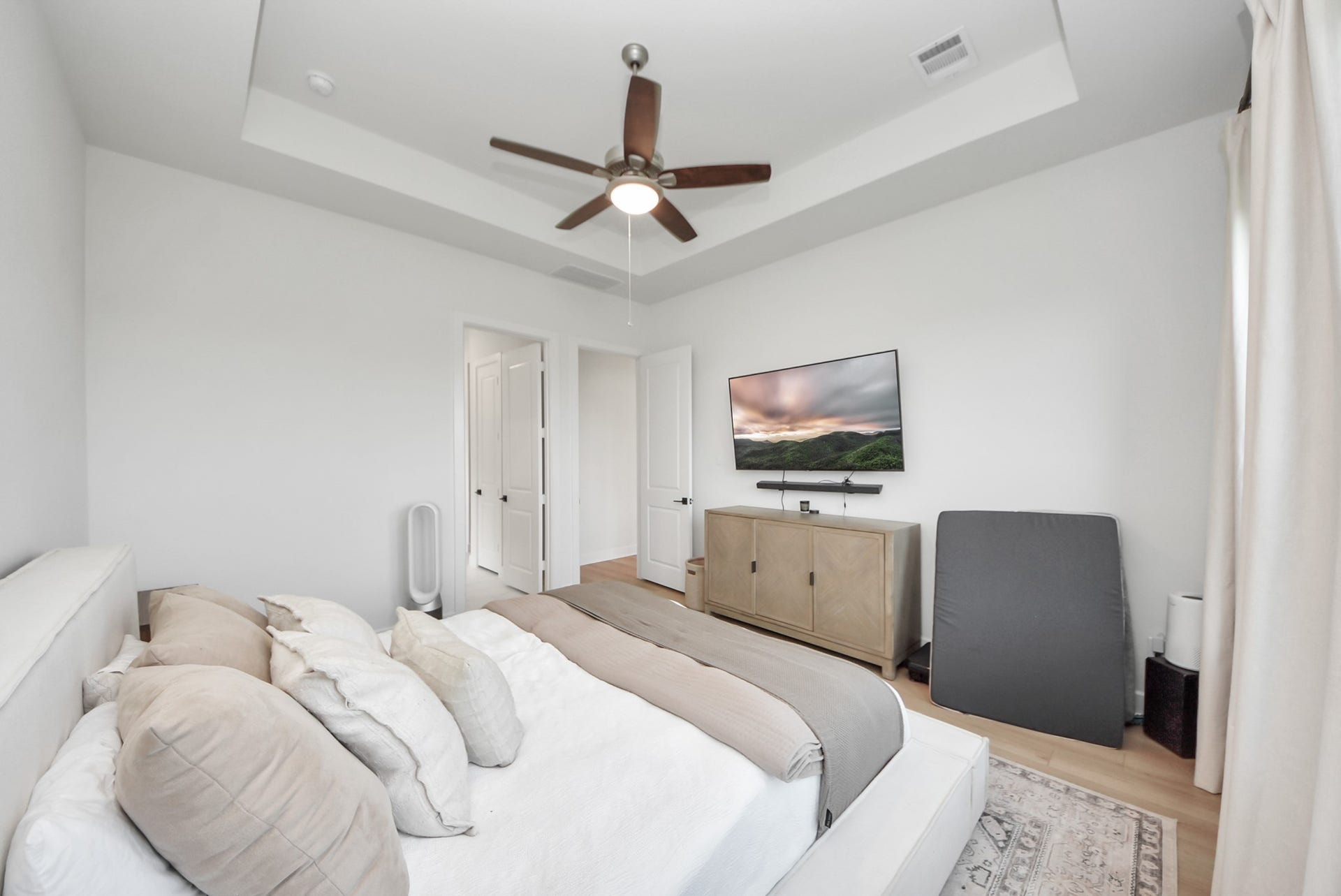 2995 Tantara Drive, Katy, TX 77493 Spacious bedroom featuring a tray ceiling with a modern fan, a wall-mounted TV, and elegant neutral decor for a serene atmosphere.