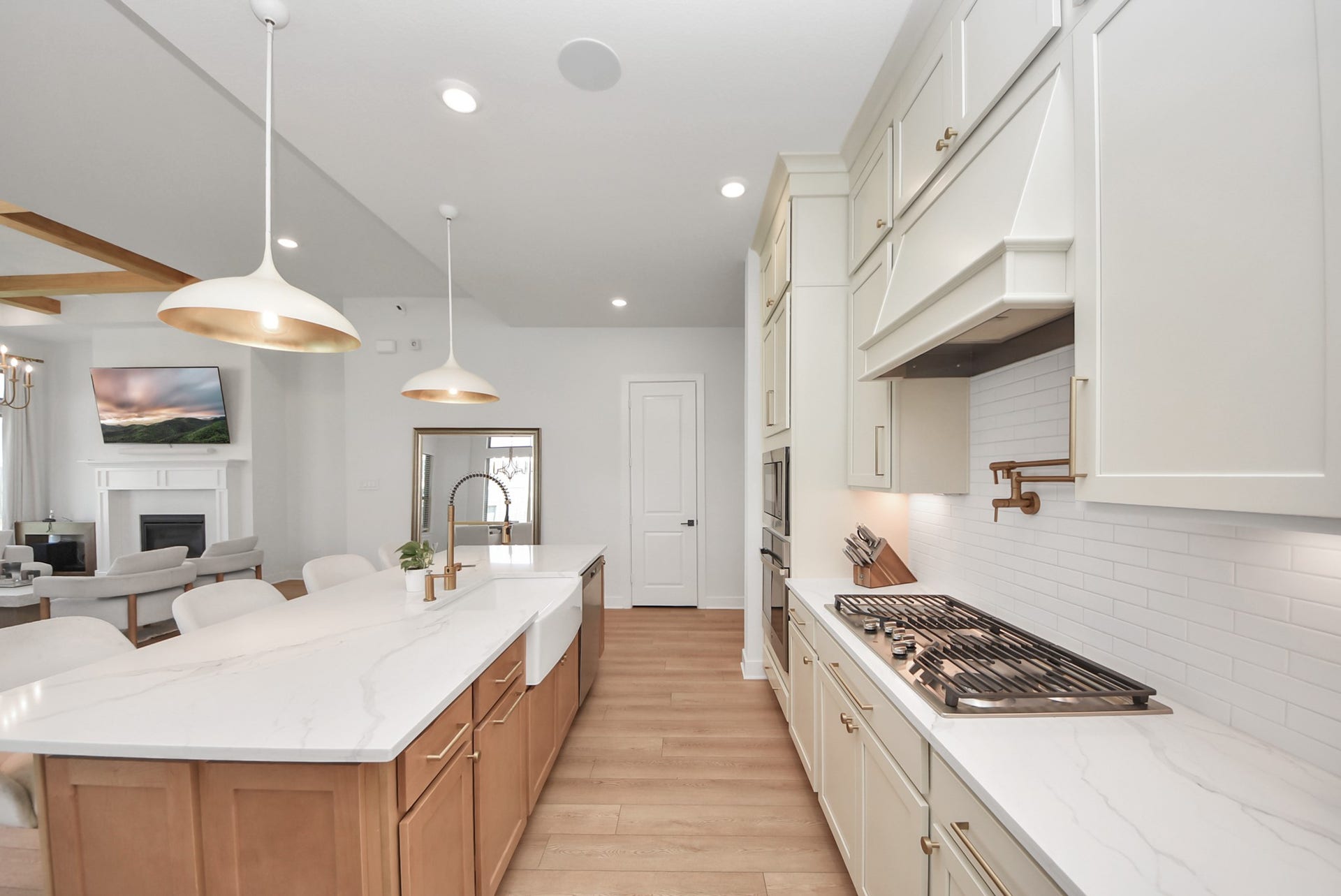 2995 Tantara Drive, Katy, TX 77493 Elegant kitchen with sleek white cabinetry, a spacious island with seating, and modern pendant lighting. The open-concept design flows into a cozy living area featuring a fireplace and a mounted TV.