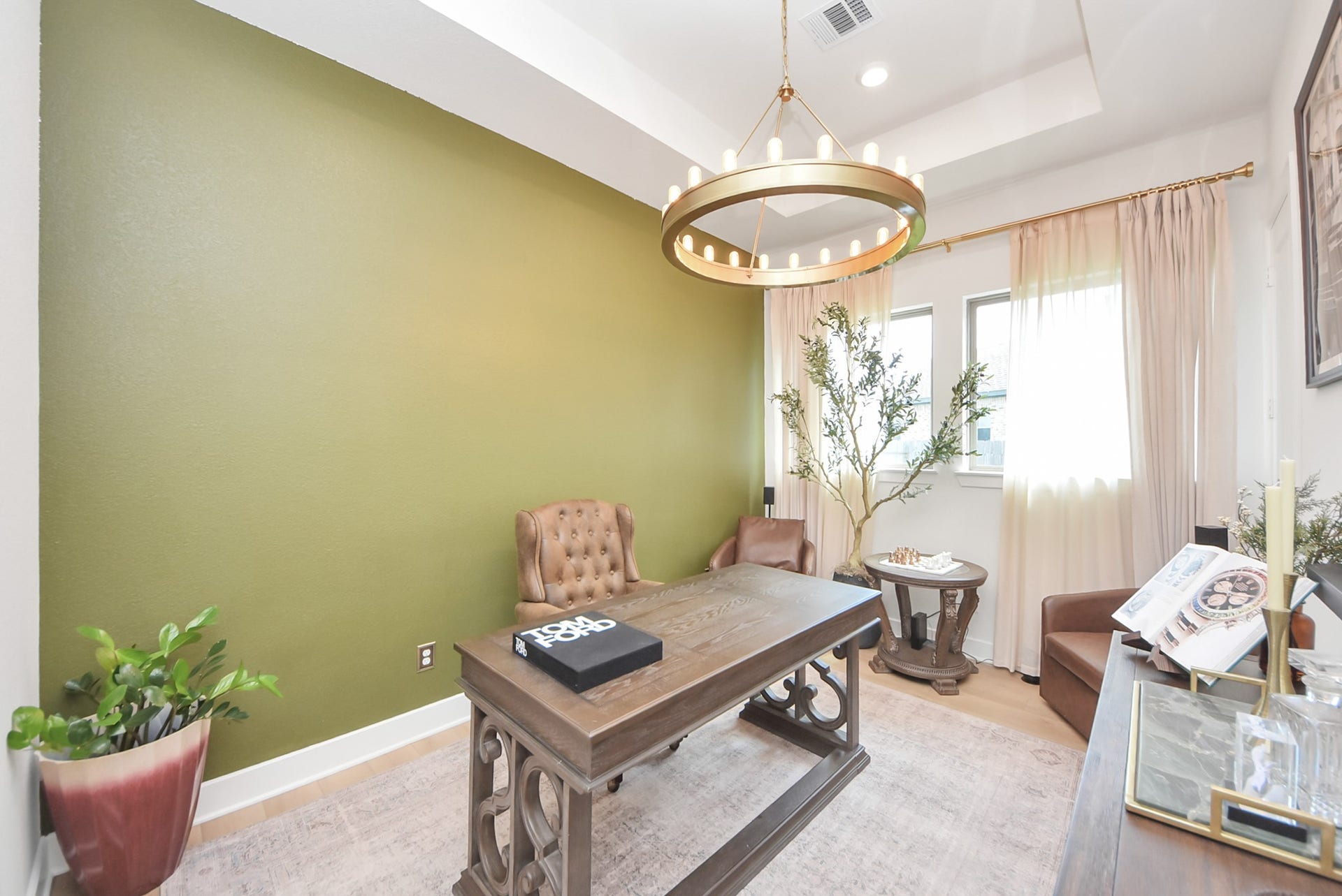2995 Tantara Drive, Katy, TX 77493 Elegant home office featuring a sophisticated wood desk, plush leather chair, and a striking green accent wall. Natural light pours in through large windows, highlighting the modern chandelier and tasteful decor.