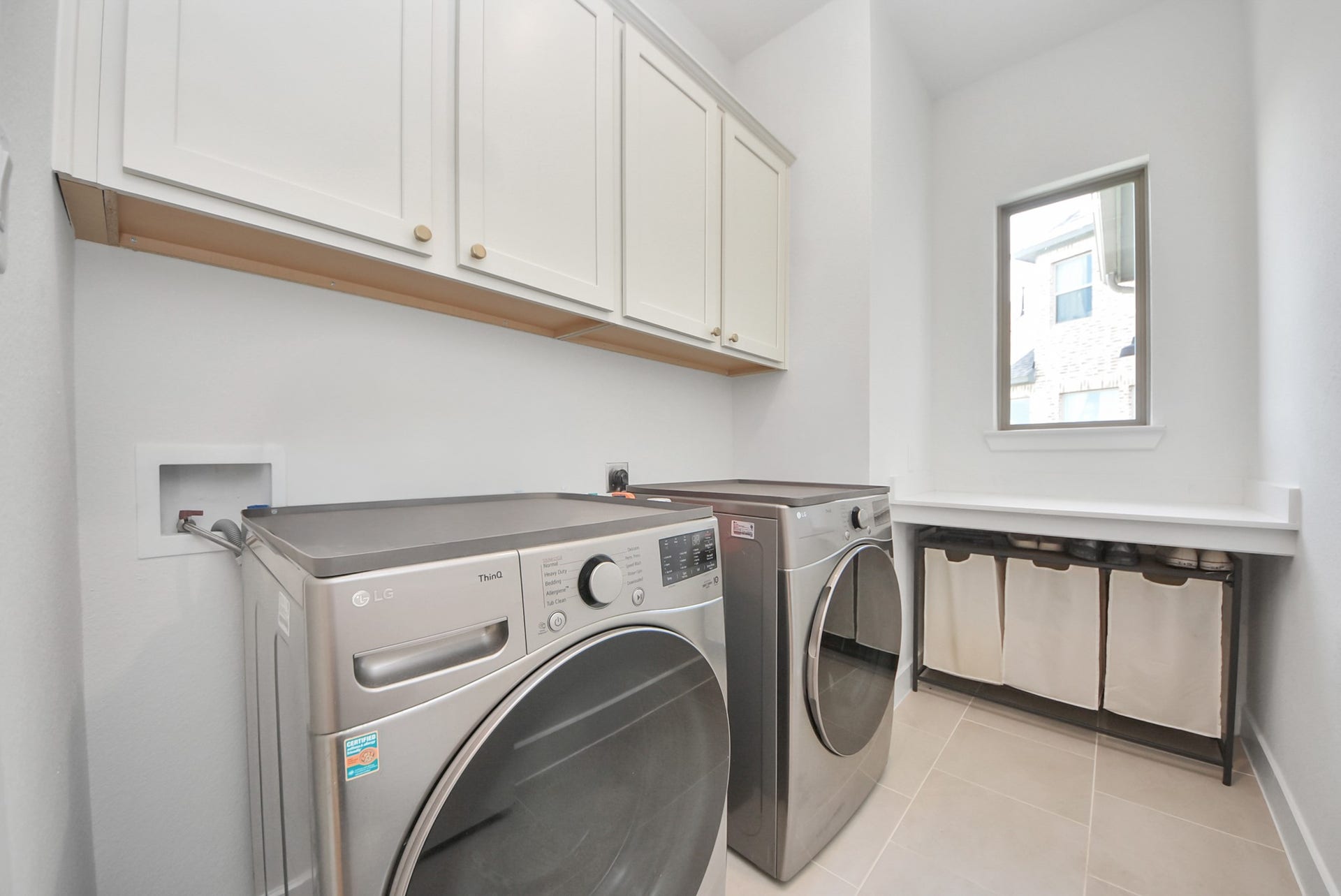 2995 Tantara Drive, Katy, TX 77493 Modern laundry room featuring sleek stainless steel washer and dryer, ample cabinetry for storage, and a convenient folding station by a bright window.