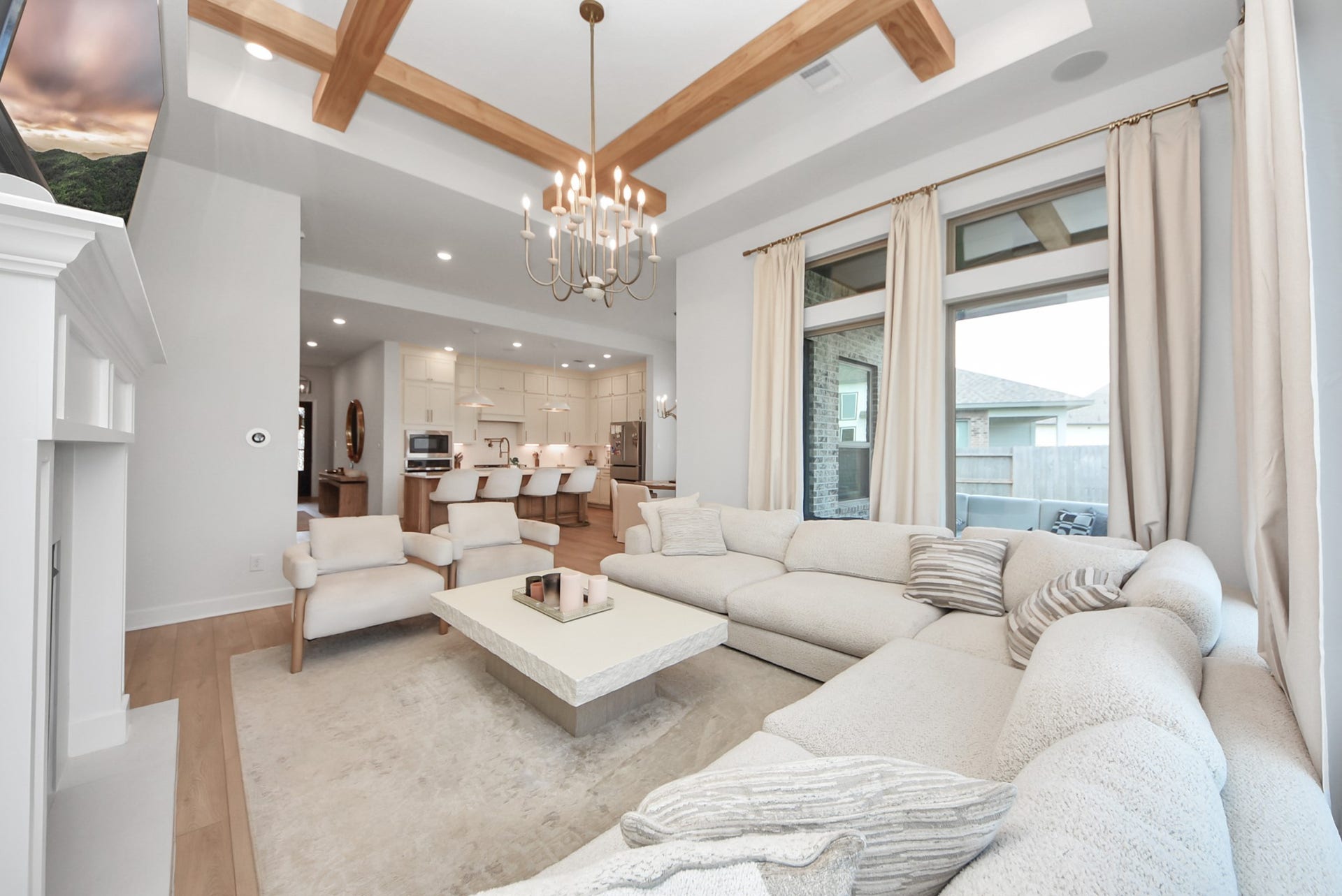 2995 Tantara Drive, Katy, TX 77493 Spacious living area with elegant wood beam accents and a cozy sectional sofa, seamlessly flowing into a modern kitchen with a large island and stylish lighting.