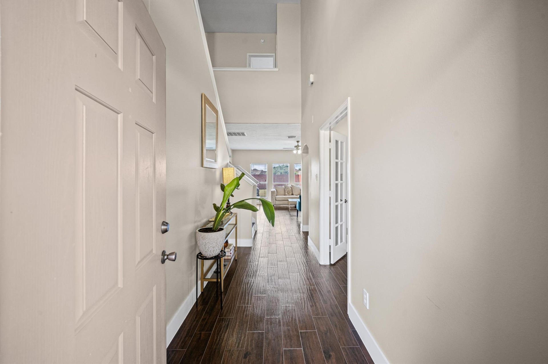 8711 Sandusky Court, Tomball, TX 77375 This photo shows a welcoming entryway with wood-look flooring and neutral-colored walls. A plant and decorative items sit on a small table, leading to a bright living area with natural light and a glimpse of a cozy seating space.