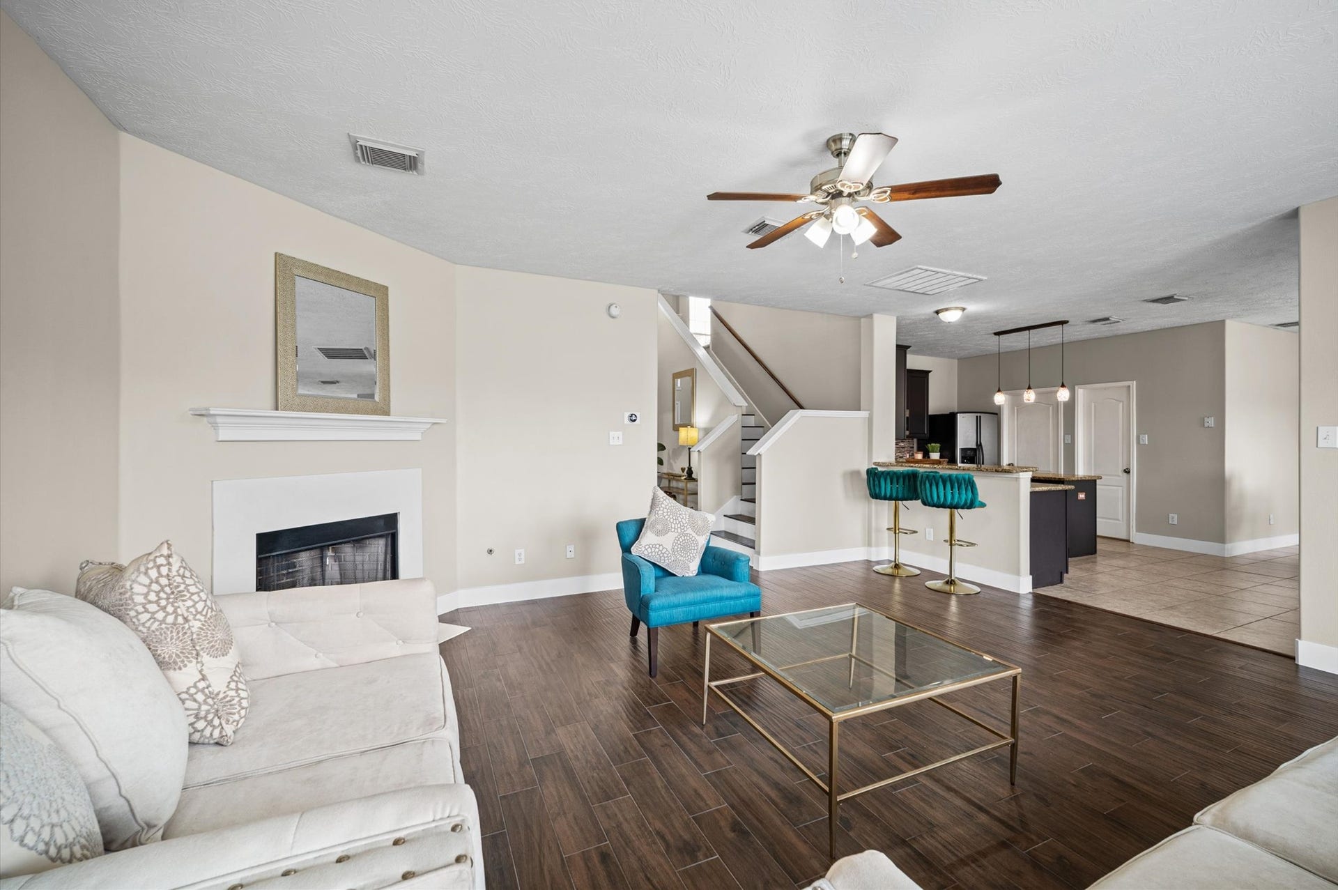 8711 Sandusky Court, Tomball, TX 77375 Bright, open-plan living space with hardwood floors, a cozy fireplace, and a modern kitchen featuring a breakfast bar. The area is complemented by a ceiling fan and stylish furnishings, perfect for comfortable living and entertaining.