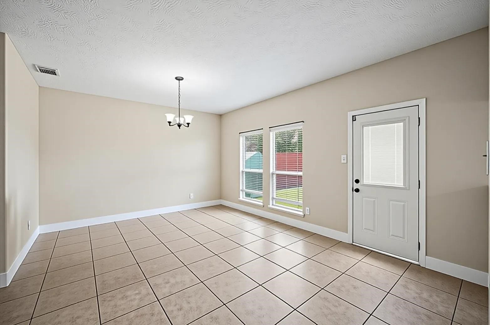 8711 Sandusky Court, Tomball, TX 77375 This dining room features tiled flooring, neutral beige walls, and a modern light fixture. It includes two large windows and a door leading outside, allowing for ample natural light. Ideal for a dining area or flexible living space.