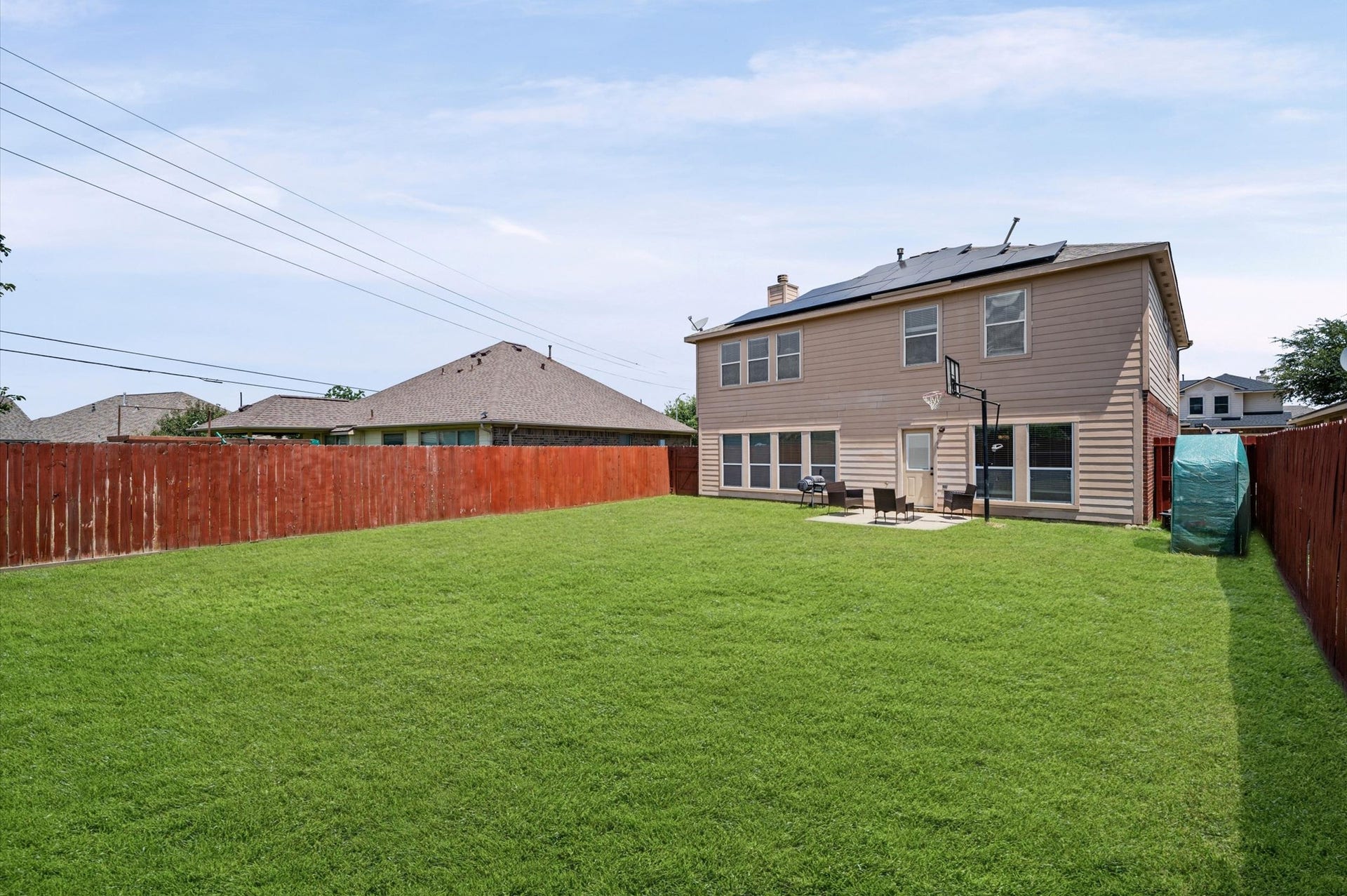 8711 Sandusky Court, Tomball, TX 77375 Spacious backyard with a well-maintained lawn, red wooden fence, and a two-story house featuring large windows and a small patio area. Ideal for outdoor activities and relaxation.