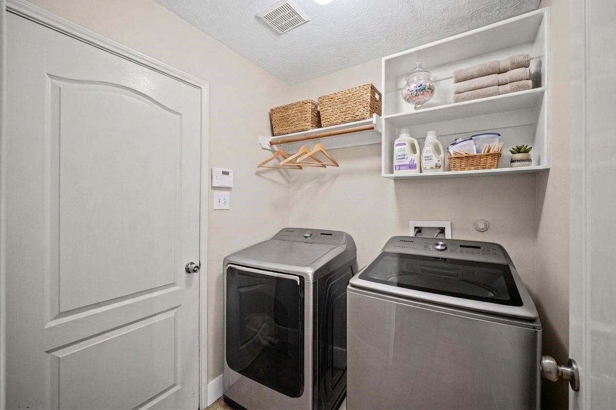 8711 Sandusky Court, Tomball, TX 77375 This photo shows a well-organized laundry room featuring modern washer and dryer units. It includes open shelving for storage, a rod for hanging clothes, and a clean, neutral color scheme.