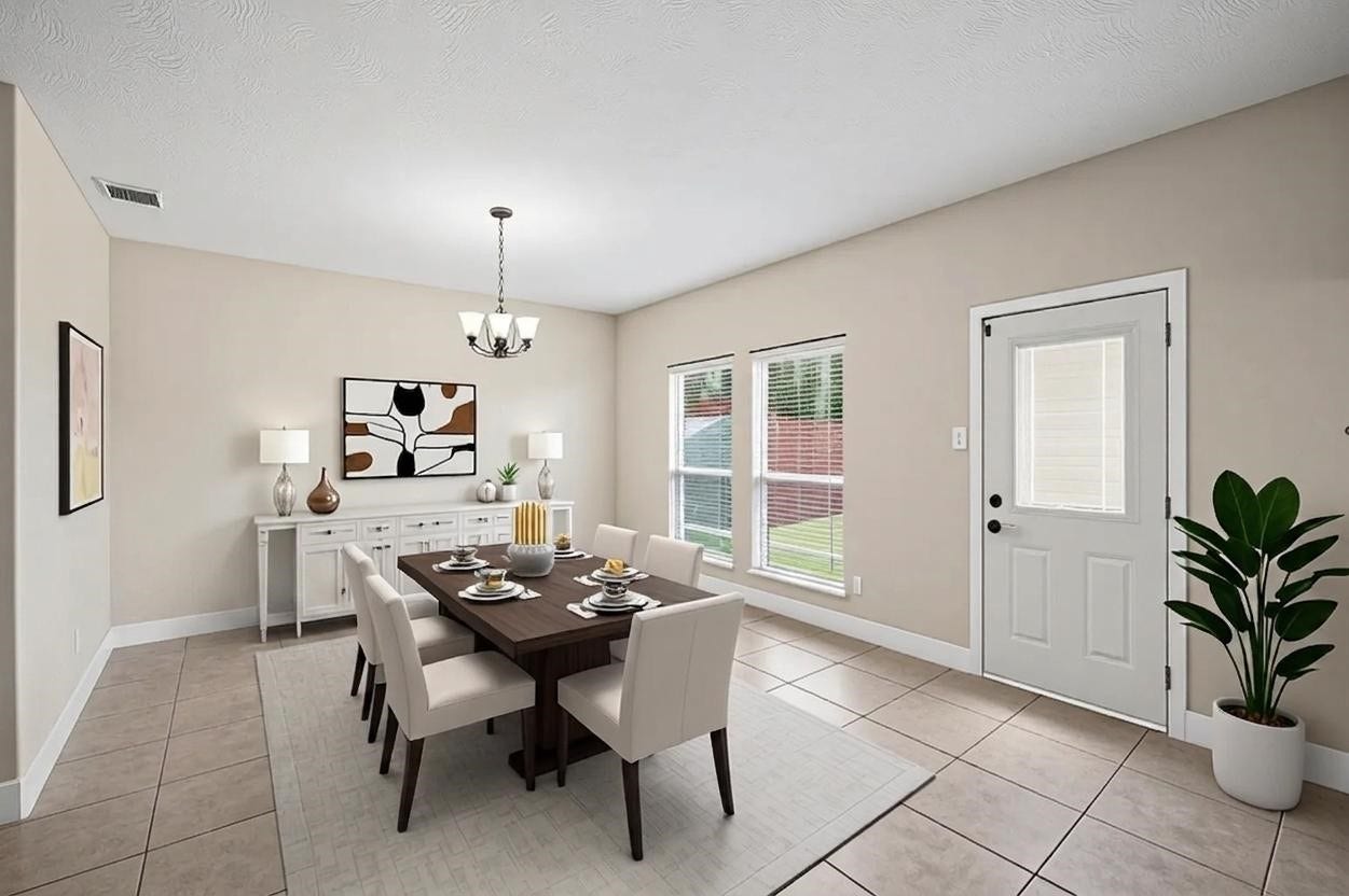 8711 Sandusky Court, Tomball, TX 77375 This photo showcases a bright dining room with neutral walls and tiled floors. It features a modern chandelier, ample natural light from two windows and a nearby door, creating a warm, inviting atmosphere.