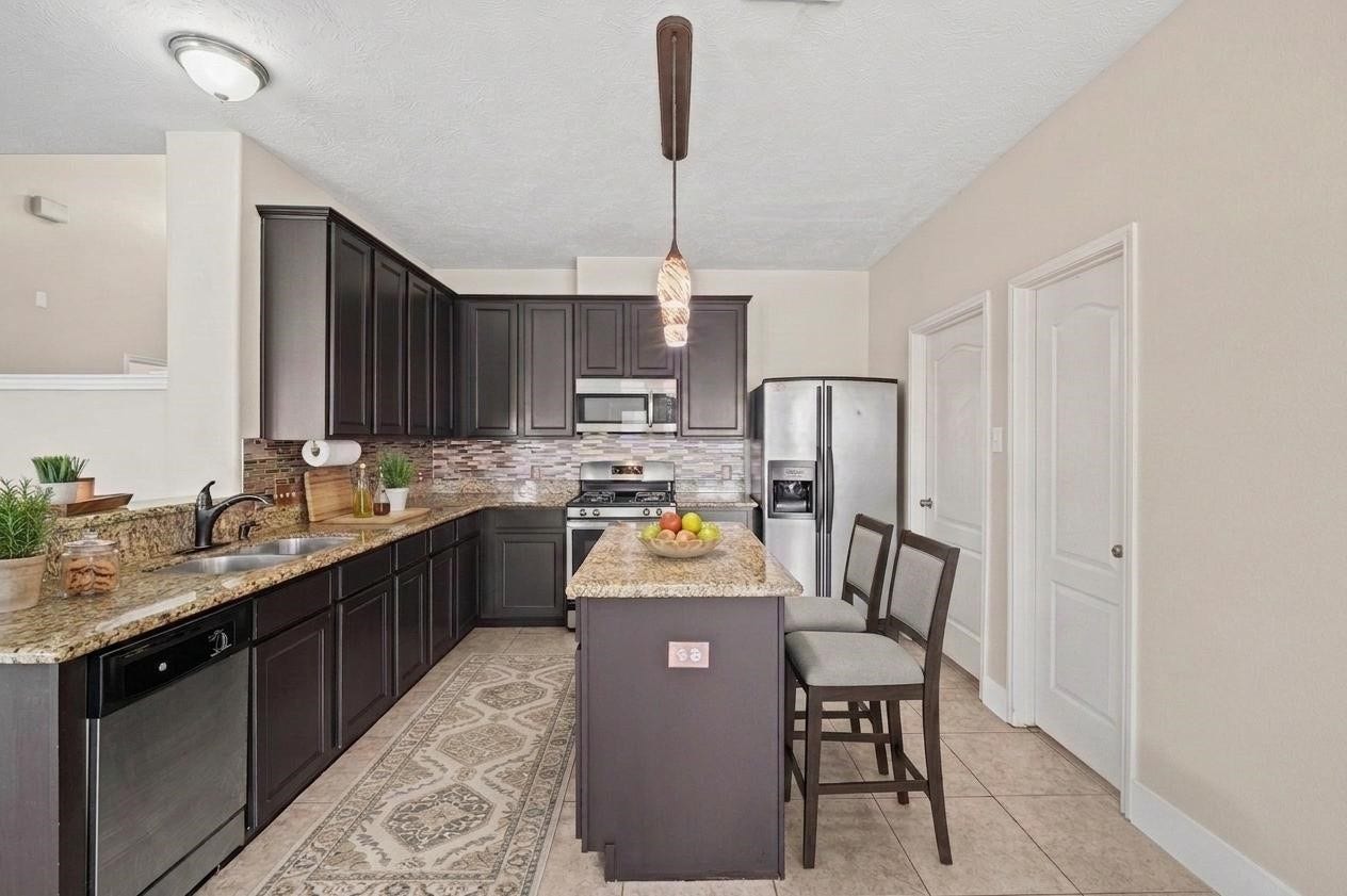 8711 Sandusky Court, Tomball, TX 77375 Modern kitchen with dark wood cabinetry, granite countertops, and tile flooring. Features include a central island, stainless steel appliances, and a stylish backsplash.