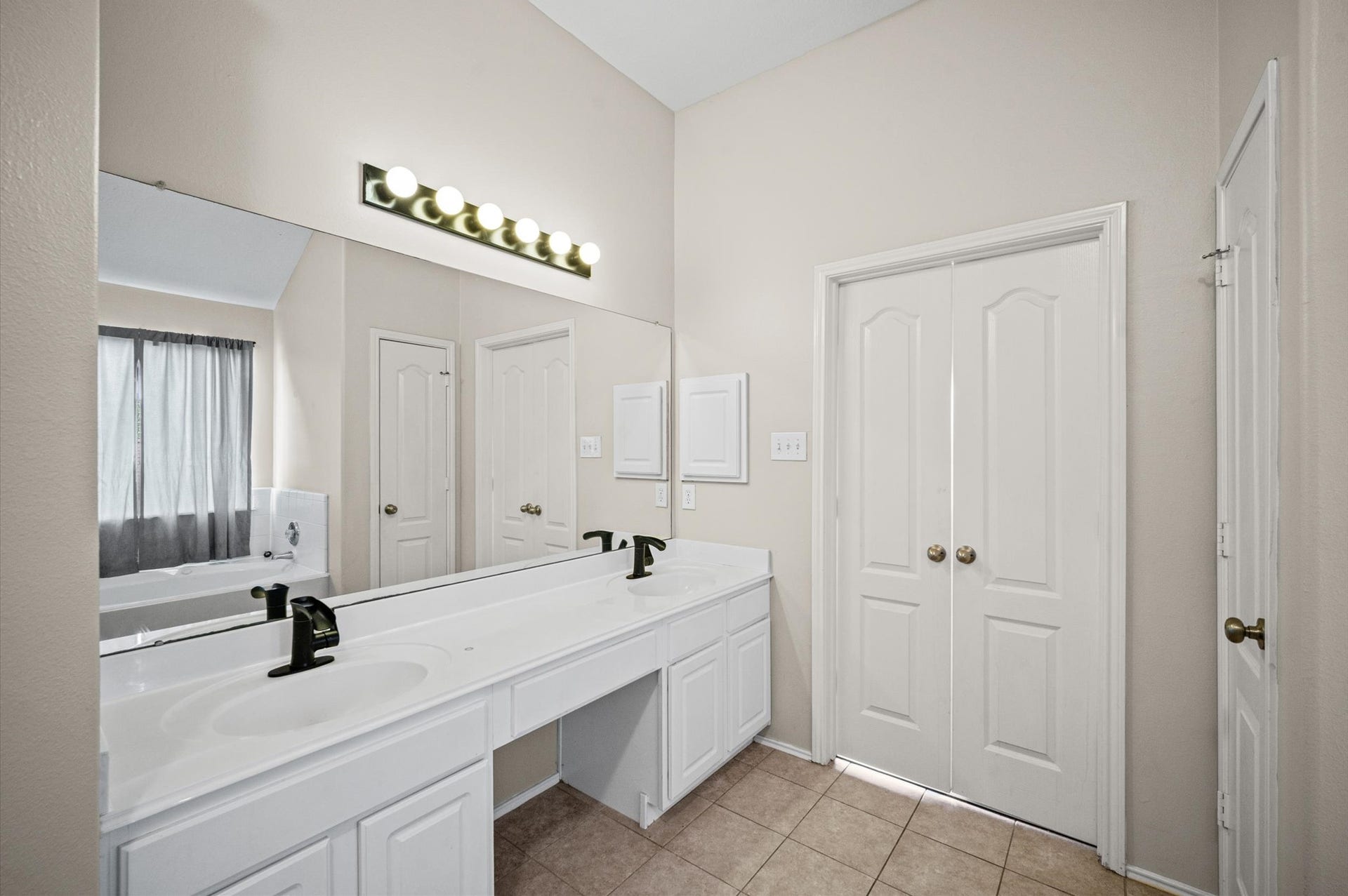 8711 Sandusky Court, Tomball, TX 77375 This bathroom features a dual-sink vanity with modern black fixtures, large mirror, bright lighting, and a separate bathtub area. It has neutral tones and ample storage, creating a clean and spacious feel.