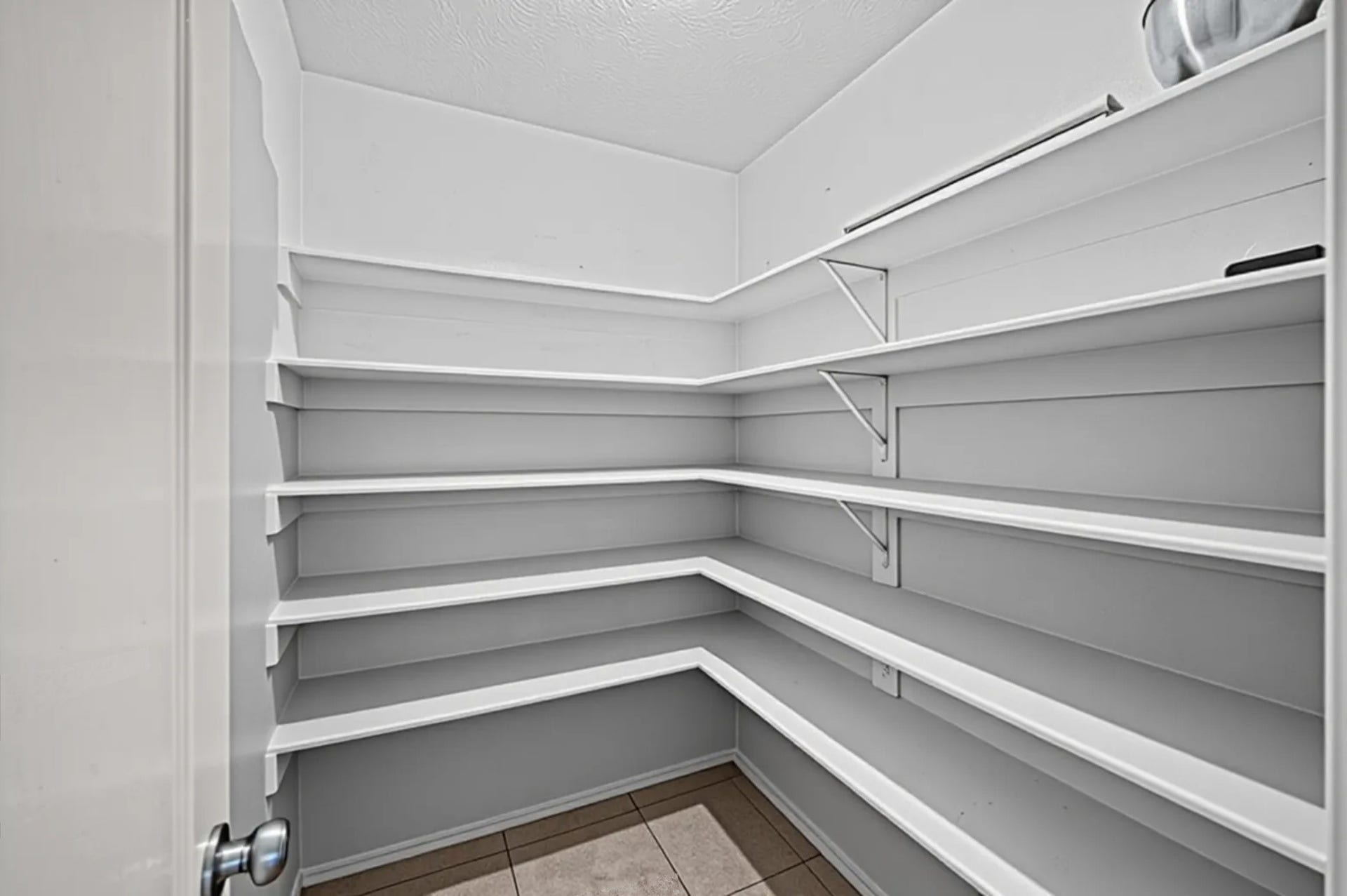 8711 Sandusky Court, Tomball, TX 77375 This photo shows a spacious pantry with multiple white shelves, ideal for organized storage. The tiled floor adds a clean, modern touch.
