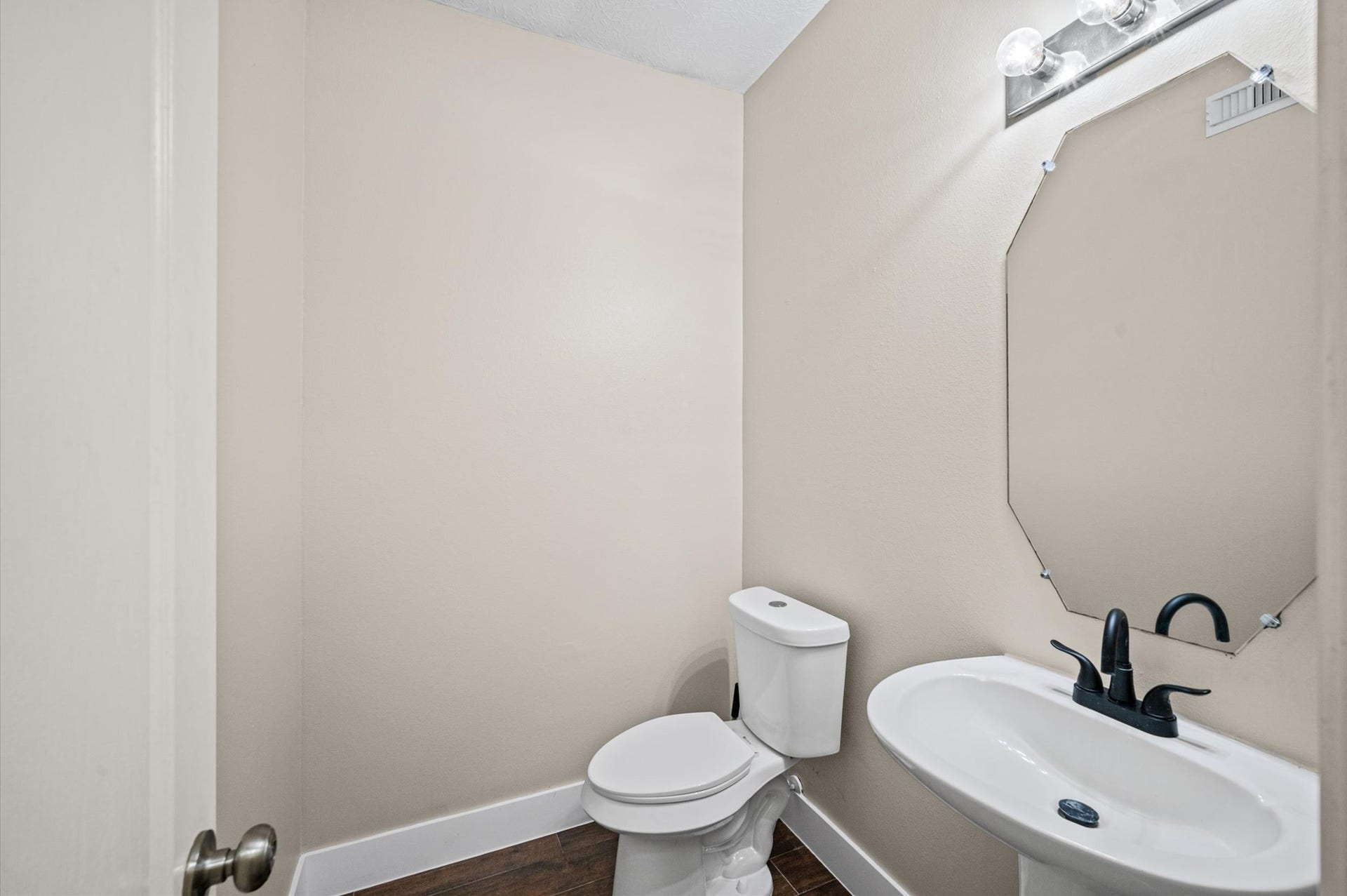 8711 Sandusky Court, Tomball, TX 77375 This is a small, modern half-bathroom with a toilet and a pedestal sink. It features a wall-mounted mirror, light fixtures above, and neutral-toned walls.
