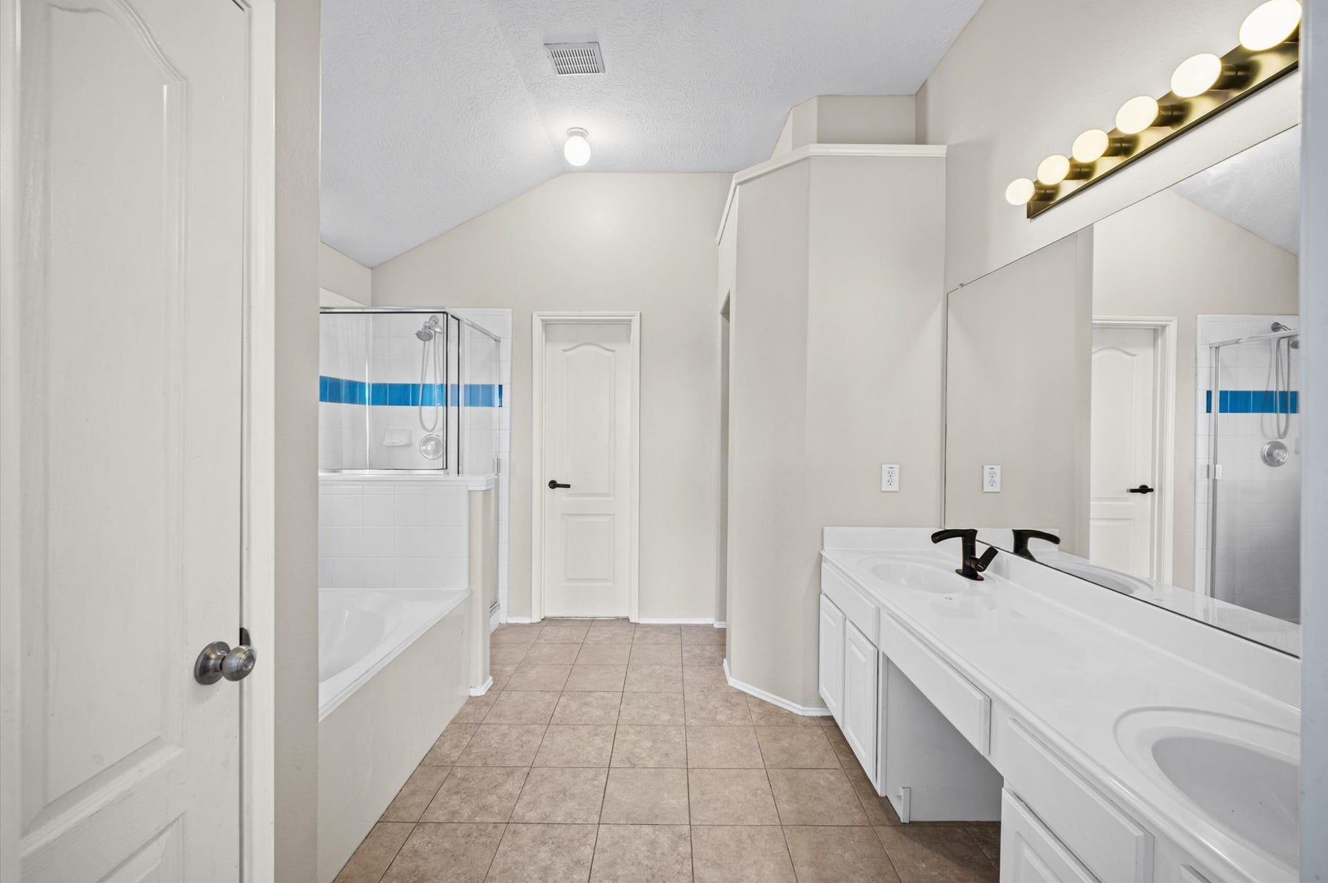8711 Sandusky Court, Tomball, TX 77375 This spacious bathroom features a double vanity, a large mirror with modern lighting, a bathtub with shower, and neutral tile flooring for a clean, contemporary look.
