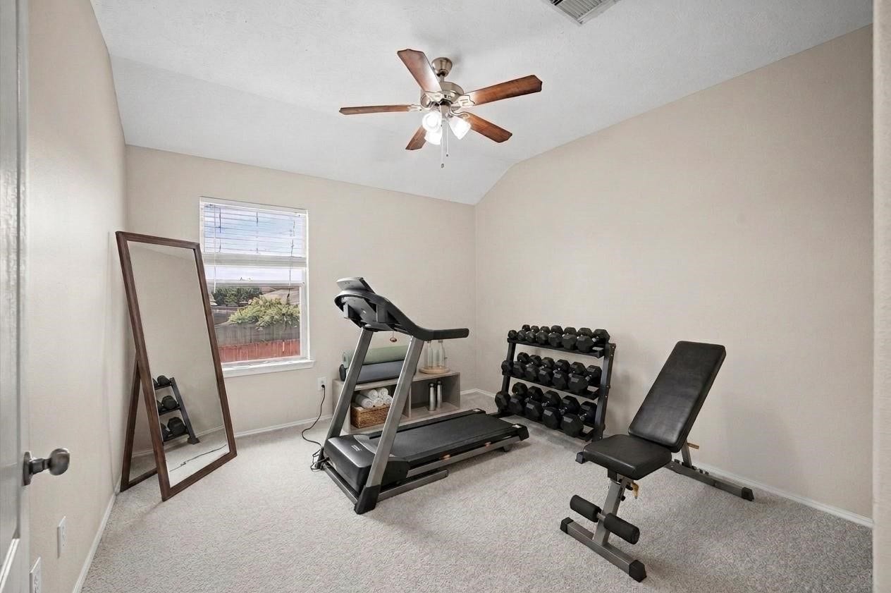8711 Sandusky Court, Tomball, TX 77375 This 4th room is set up as a home gym, featuring a treadmill, adjustable bench, and dumbbell rack. It has carpeted flooring, neutral walls, a ceiling fan, and a window with natural light.