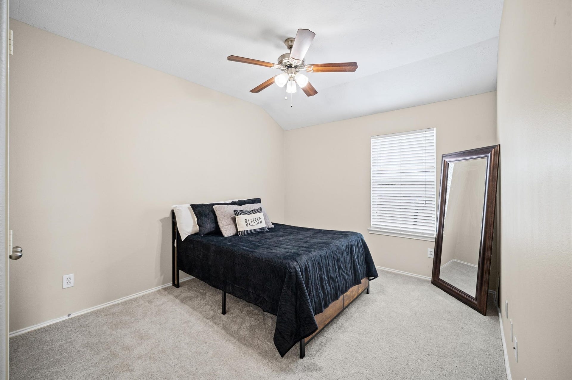 8711 Sandusky Court, Tomball, TX 77375 This is a cozy bedroom featuring neutral walls, a ceiling fan, and a window providing natural light. It includes a bed and a large mirror, offering a simple and inviting space.
