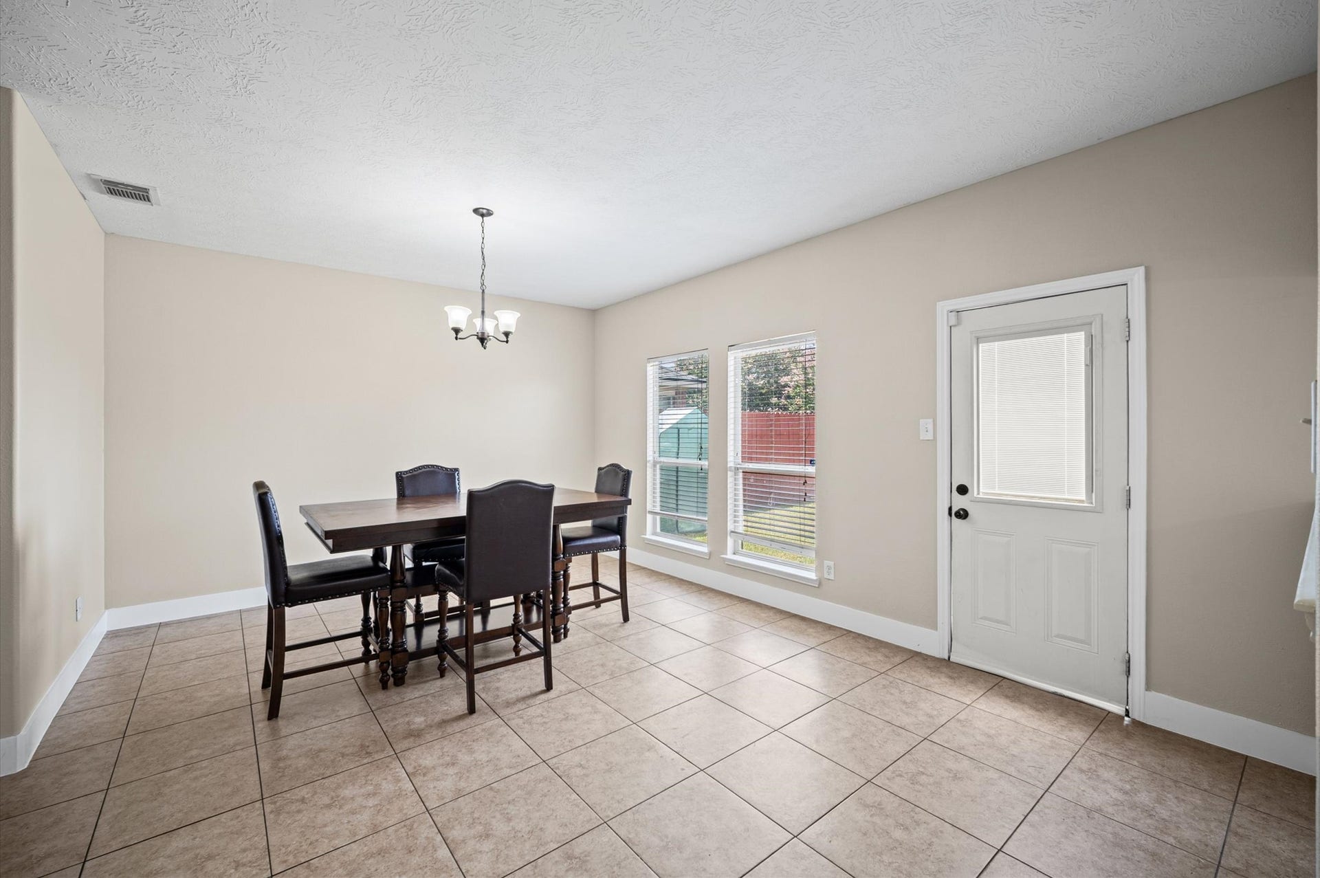 8711 Sandusky Court, Tomball, TX 77375 Bright dining area with tiled floors, neutral walls, and large windows offering natural light. Features a stylish chandelier, a door leading outside, and a cozy table setting. Perfect for family meals and entertaining.