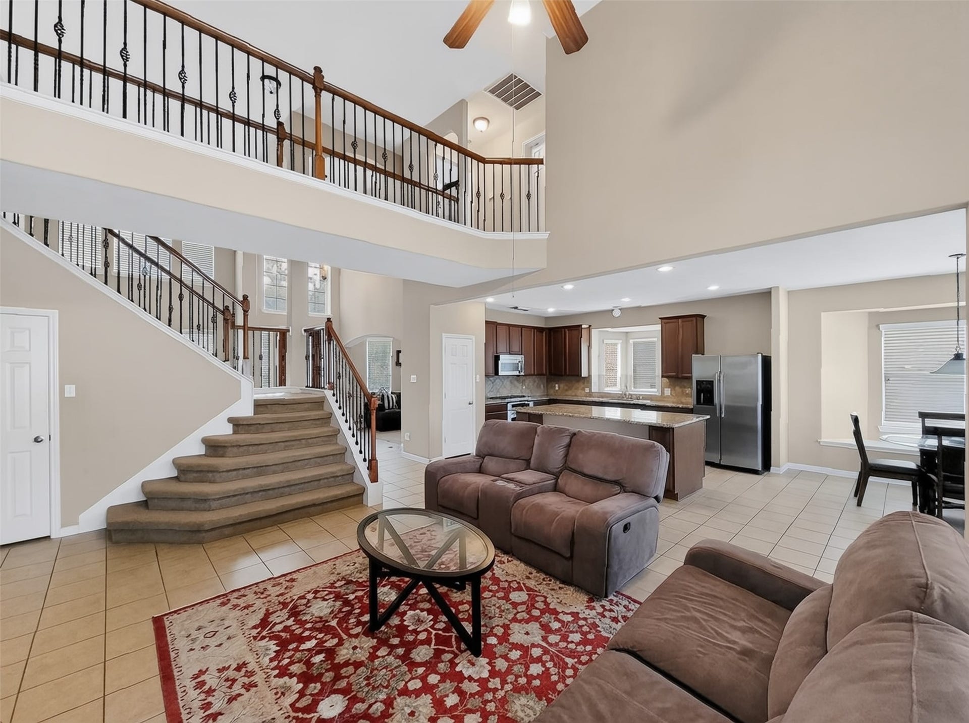 2006 Linden Cove Court, Katy, TX 77494 Spacious open-concept living area featuring a cozy seating arrangement, elegant staircase with wrought-iron railing, and a modern kitchen with stainless steel appliances and a central island.
