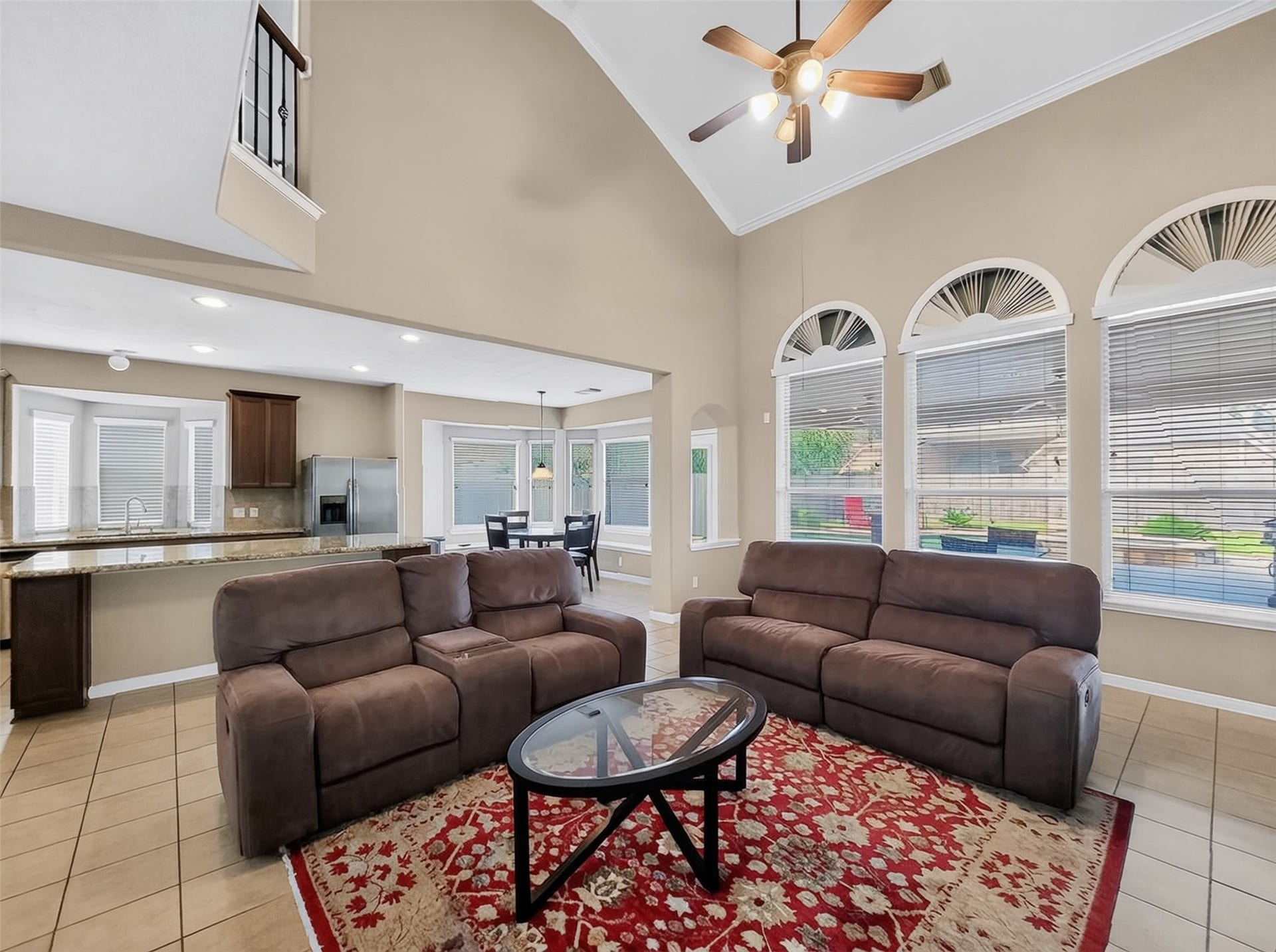 2006 Linden Cove Court, Katy, TX 77494 Spacious living area with high ceilings, featuring large arched windows for ample natural light, an open layout connecting to a modern kitchen with granite countertops, and a cozy seating arrangement on a stylish red rug.