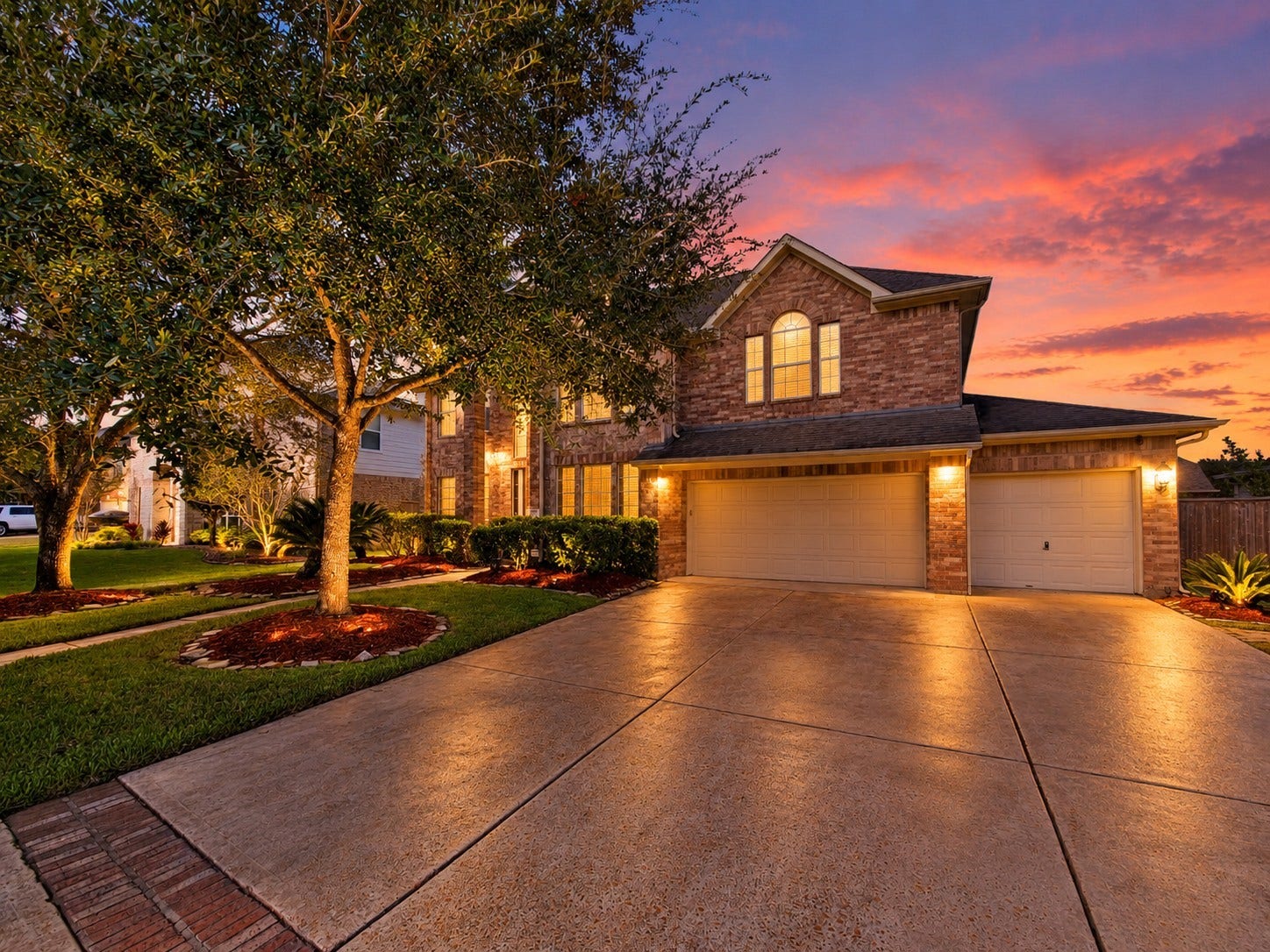 2006 Linden Cove Court, Katy, TX 77494 Stunning two-story brick home with a spacious three-car garage, beautifully lit at sunset, surrounded by lush landscaping and mature trees.