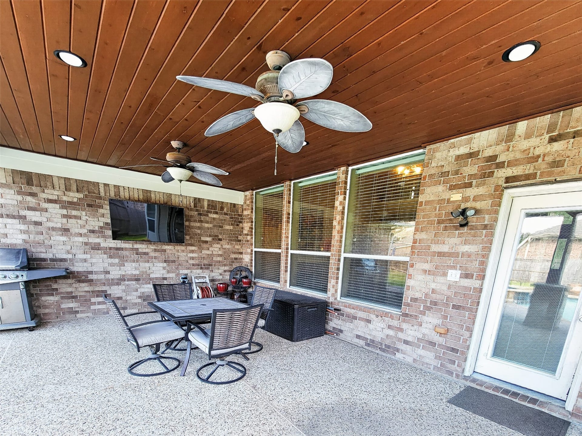 2006 Linden Cove Court, Katy, TX 77494 Spacious covered patio featuring a wood-paneled ceiling with fans, perfect for outdoor entertaining, complete with a dining area, grill, and mounted TV.