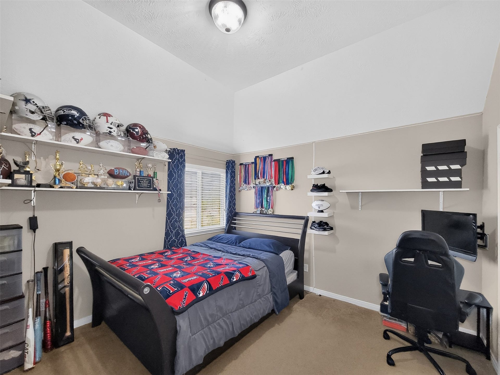 2006 Linden Cove Court, Katy, TX 77494 Cozy bedroom with sloped ceiling, featuring a comfortable bed, ample shelving for trophies and memorabilia, and a study area with a desk and chair, perfect for a young sports enthusiast.