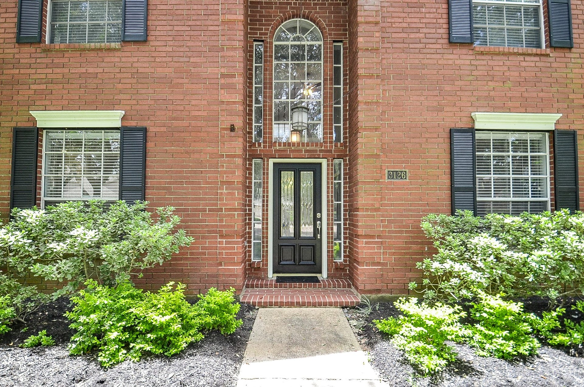 Inviting entrance with freshly painted front door and mature landscape