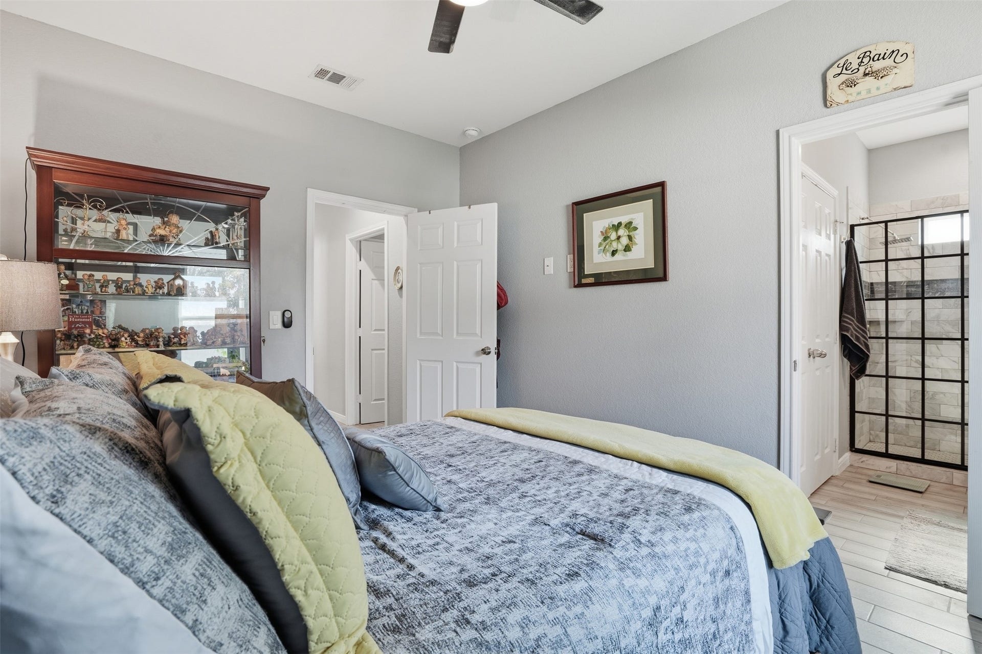 16740 Stonefield, Montgomery, TX 77316 Cozy bedroom with elegant decor, featuring a comfortable bed with layered pillows and a stylish glass display cabinet. Adjacent is a sleek en-suite bathroom with modern fixtures.
