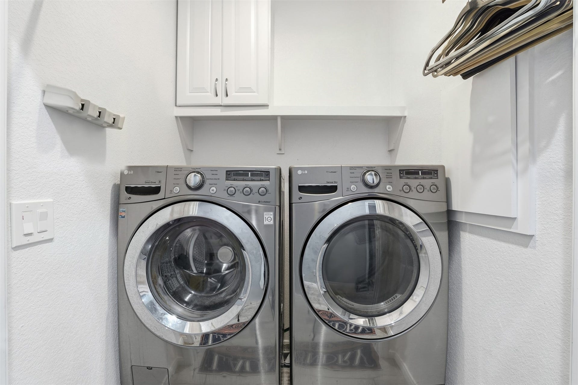 16740 Stonefield, Montgomery, TX 77316 Laundry room with sleek stainless steel front-loading washer and dryer, ample shelving, and cabinet space for storage.