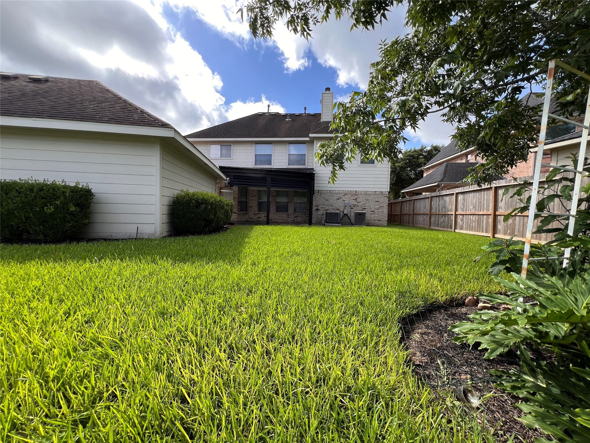 908 Azalea Pointe, League City, TX 77573 Spacious backyard with lush green lawn, mature trees, and a charming two-story home featuring a covered patio, perfect for outdoor relaxation.