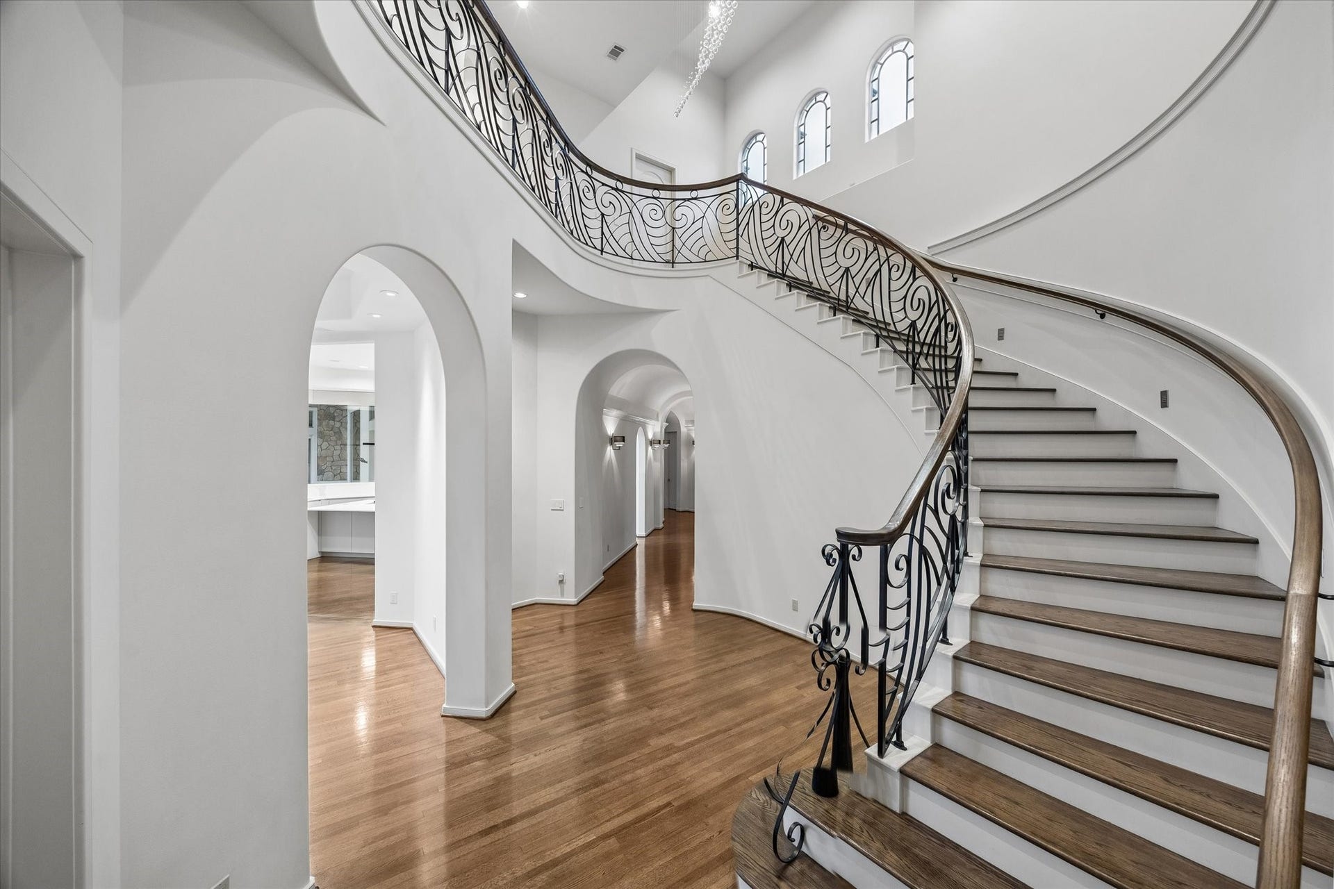 ELEGANT CURVED STAIRCASE - decorative wrought-iron balustrade and wood treads - note that the theme of arches is carried throughout the home - views into the family room, kitchen and down the long hallway to the front entry foyer