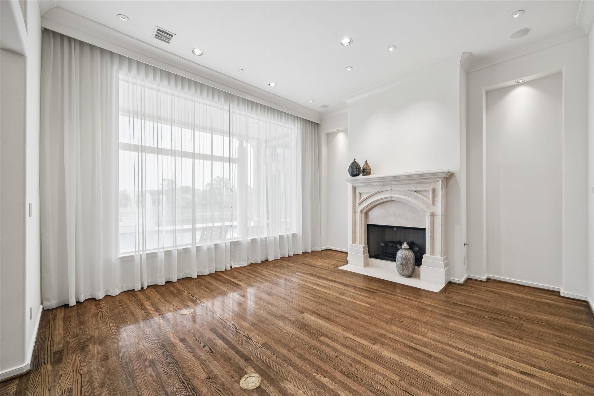 FORMAL LIVING ROOM WITH CLASSIC MANTEL SURROUND FOR GAS-LOG FIREPLACE - fireplace flanked by lighted art niches, handsome hardwood flooring, sheer draperies on the wide panoramic window overlooking the pool/spa and lake - providing beautiful views throughout the day