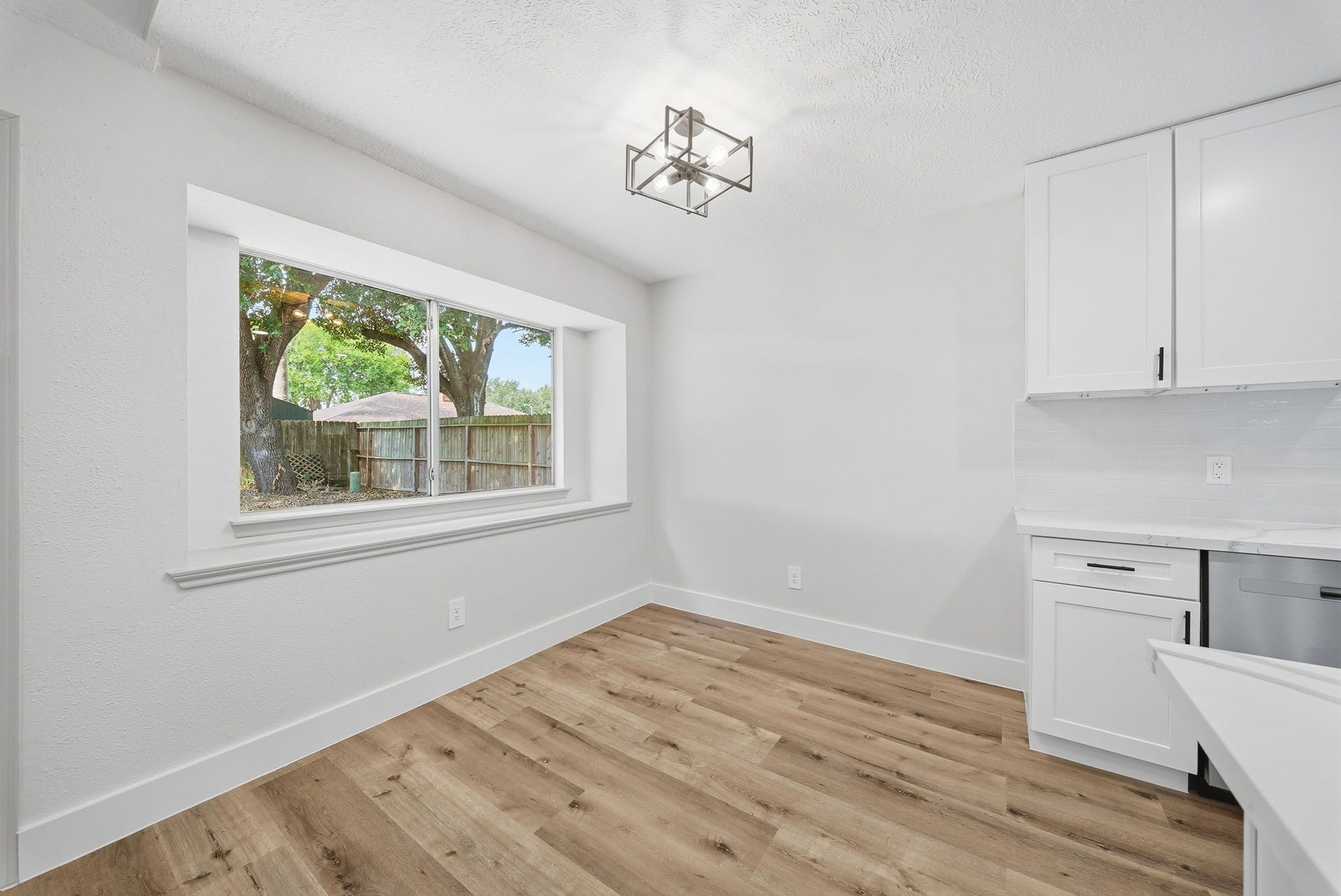 3816 Youpon Drive, La Porte, TX 77571 Bright and inviting kitchen area featuring a large bay window, modern light fixture, and sleek white cabinetry, complemented by warm LVN flooring.
