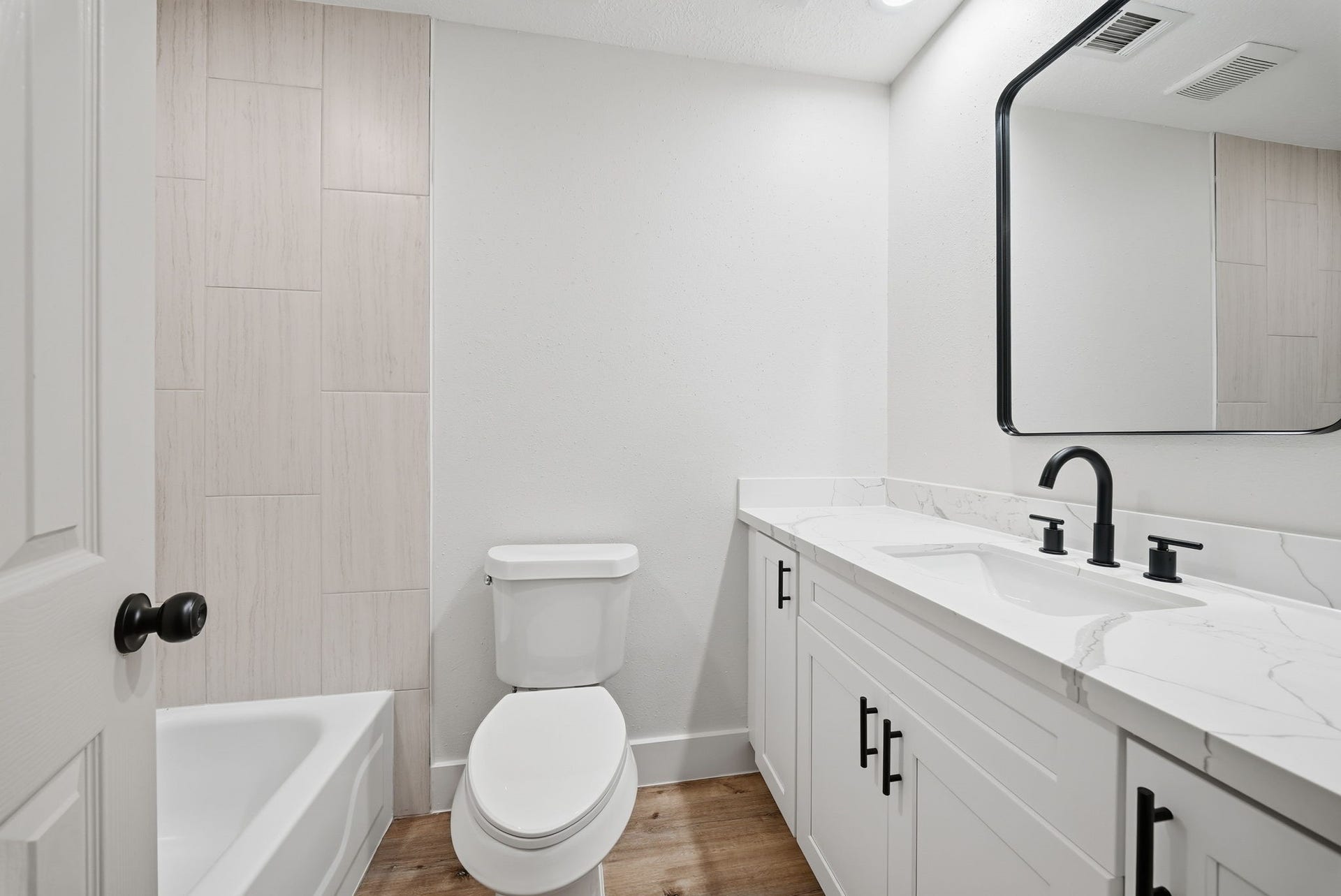 3816 Youpon Drive, La Porte, TX 77571 Modern bathroom featuring a sleek double vanity with elegant black fixtures, a spacious mirror, and a pristine bathtub surrounded by light tile accents.