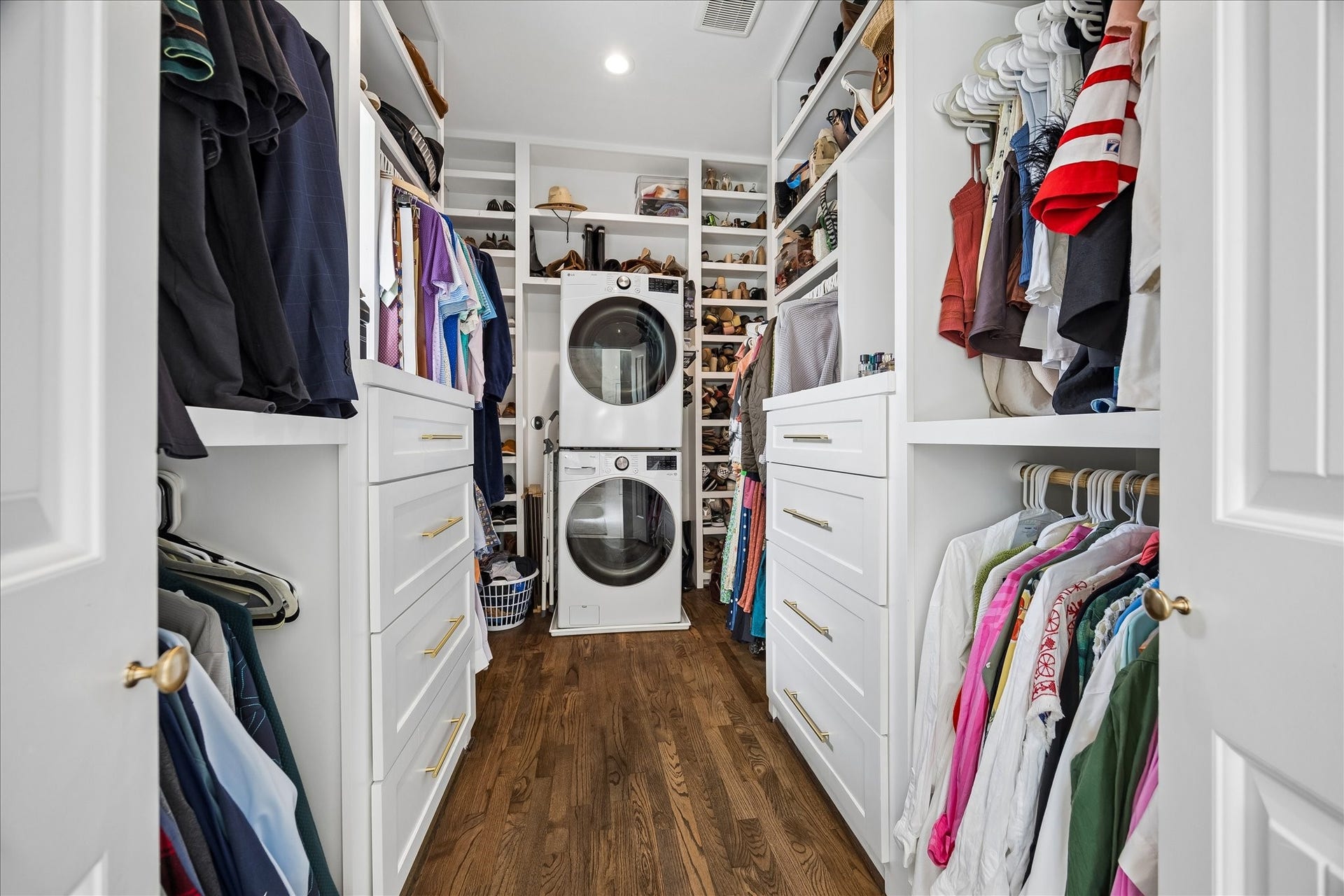 Spacious custom walk-in closet with elegant built-in cabinetry & storage, ample hanging space, drawers, and shelving, complete with included front-load washer and dryer.