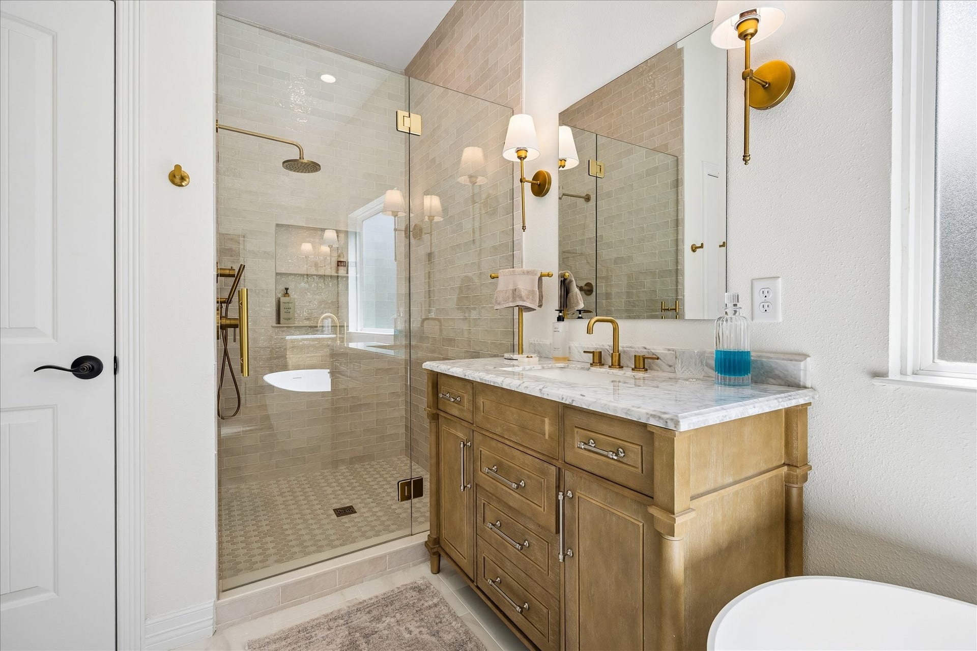Elegant bathroom featuring a spacious glass-enclosed shower with gold fixtures, his & her quartz topped vanities, and stylish lighting accents.
