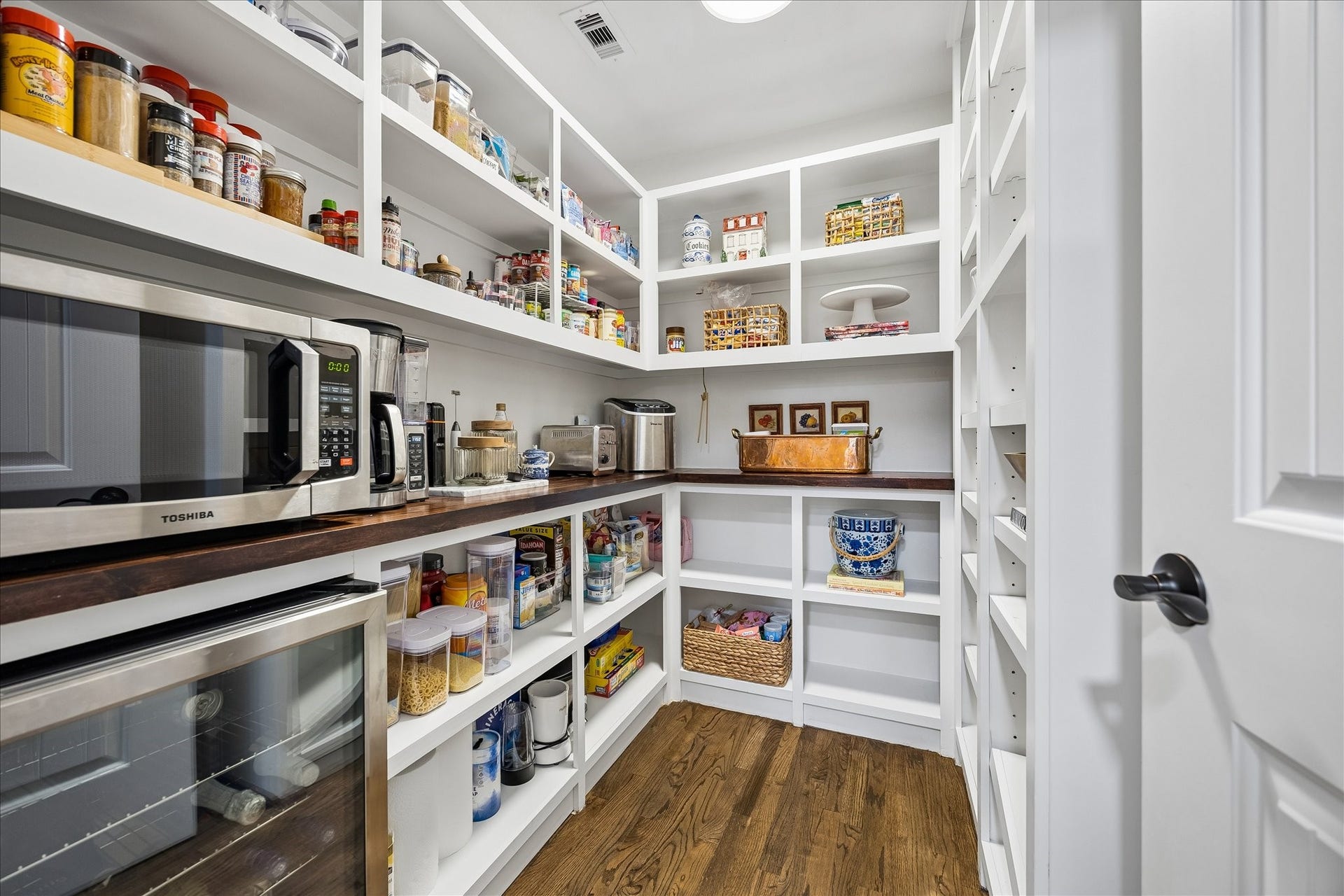 Spacious walk-in pantry with ample shelving, with shelves for microwave and kitchen appliances, perfect for maximizing storage and accessibility.