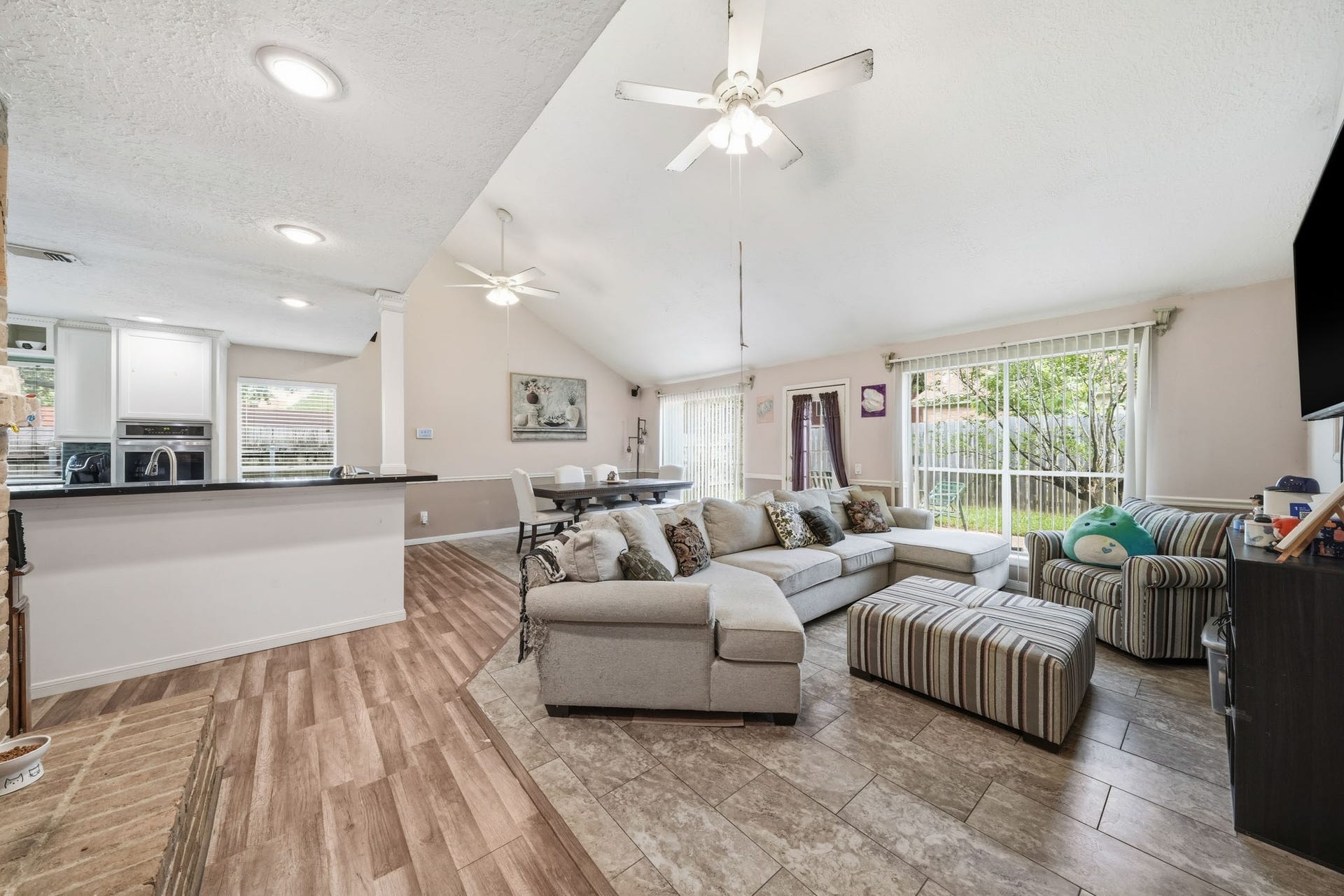 15026 Howland Street, Houston, TX 77084 View of family area from the hallway featuring a brick fireplace, tile and wood-look flooring, ceiling fans, recessed lighting and open to kitchen, family area, and dinning.