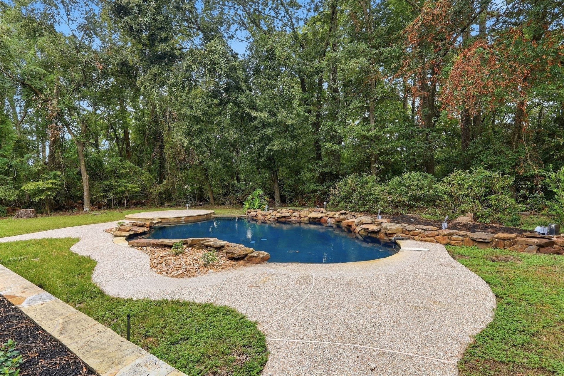 Backyard pool is surrounded by mature trees, lush greenery, and natural stone accents, creating a private, peaceful setting.