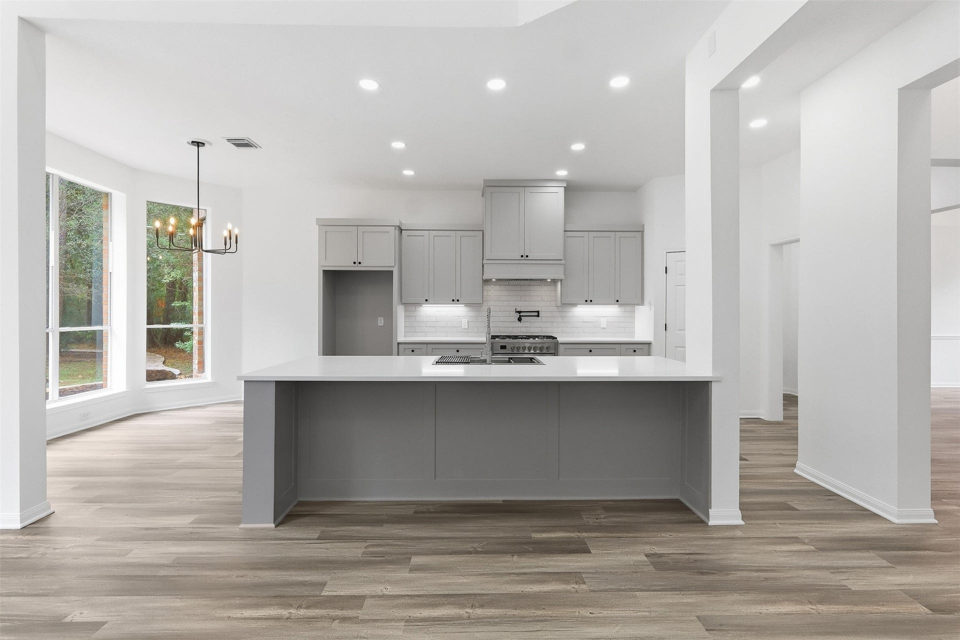 This open kitchen features light gray custom cabinetry with black hardware, white quartz countertops, and a classic white subway tile backsplash.