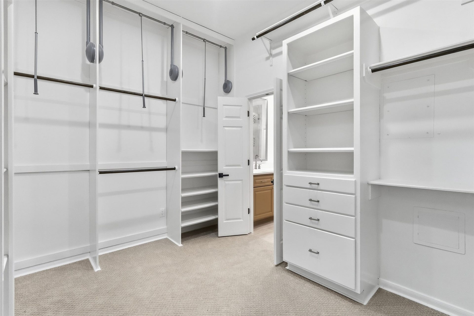Spacious primary closet with custom built-ins, multiple hanging areas, pull-down rods, and ample shelving for organized storage.
