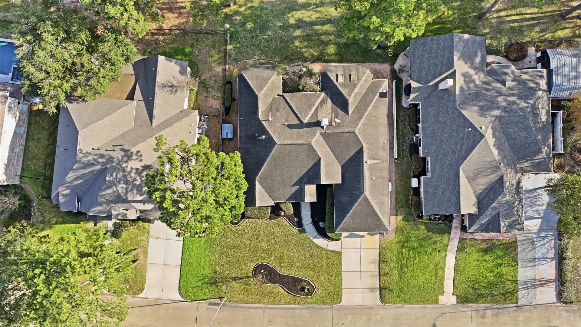 This aerial photo shows a row of three single-family homes with well-maintained lawns and driveways. The houses are evenly spaced, and the neighborhood appears green and residential, with mature trees providing shade and privacy.