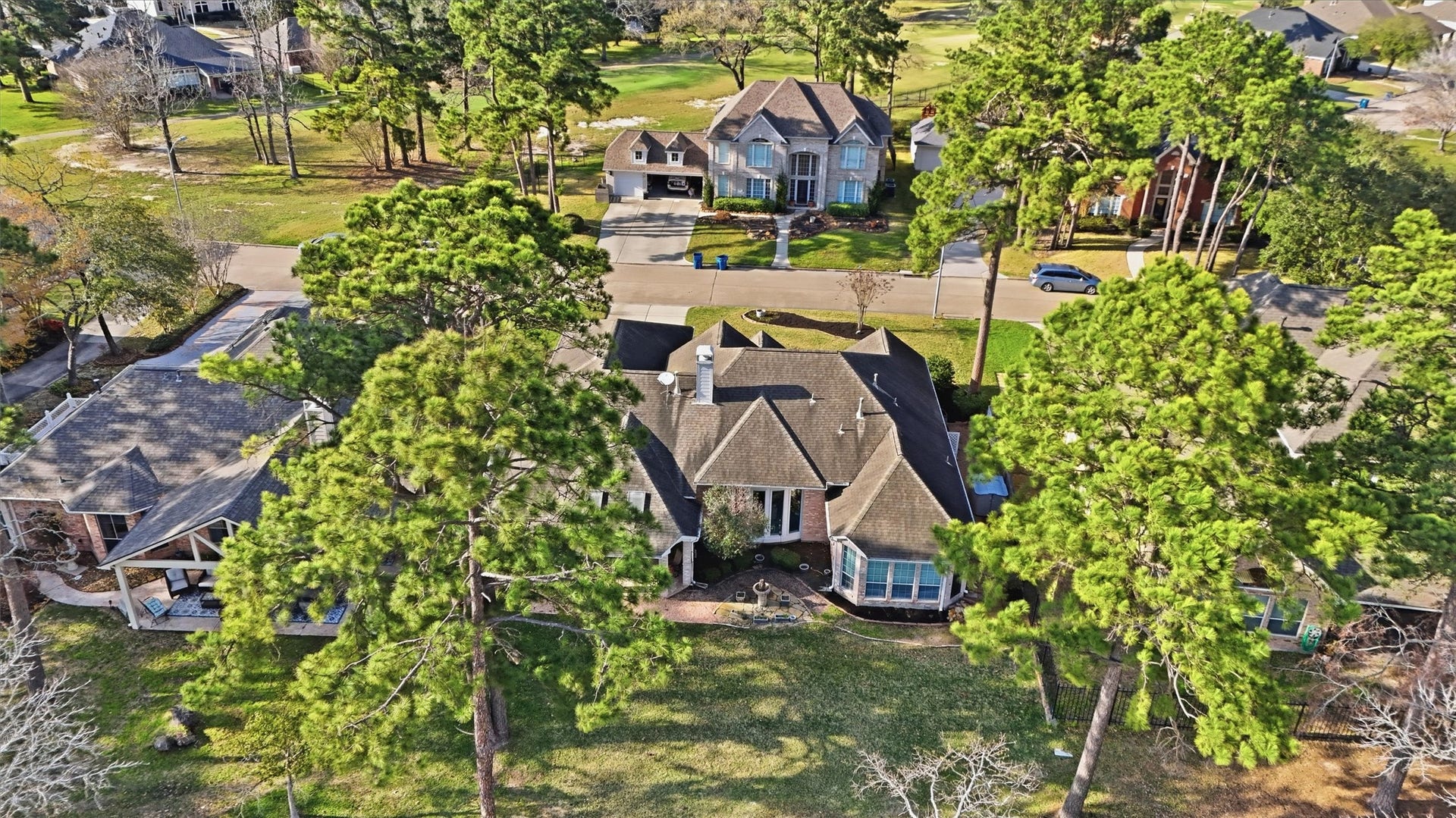 This aerial photo showcases a charming single-story home nestled among tall, mature trees. It features a well-maintained lawn and is situated in a picturesque, tree-lined neighborhood. The house has a classic design with large windows, and the surrounding area looks peaceful and inviting.