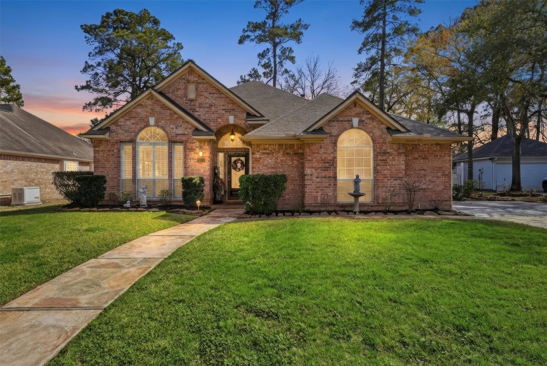 Charming brick home with a welcoming pathway, well-manicured lawn, and elegant arched windows. The cozy exterior is enhanced by a sunset backdrop, creating an inviting atmosphere.