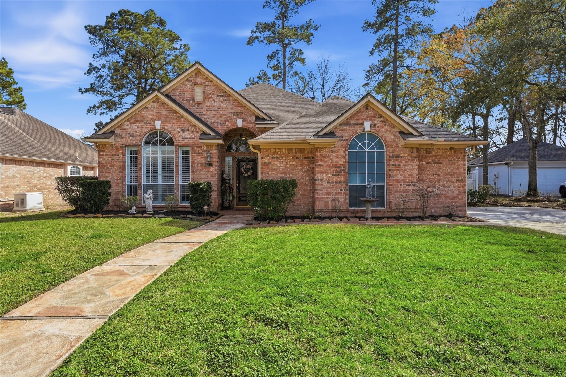 Charming brick home with a welcoming front entrance, large arched windows, and a well-maintained lawn. The property features a paved walkway and mature trees, offering a serene and inviting atmosphere.