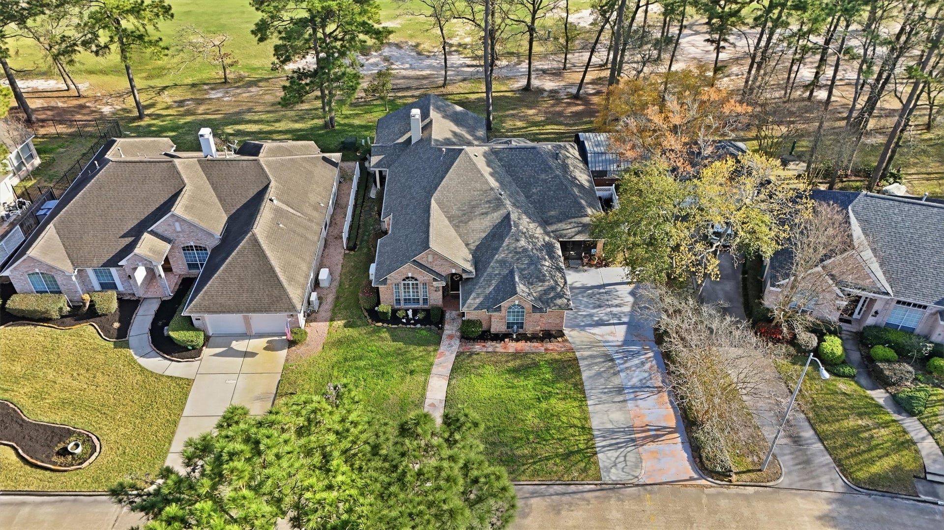 This aerial photo showcases a single-story brick home with a well-maintained lawn and a paved driveway. It's situated in a quiet neighborhood, bordered by trees and adjacent to a golf course. The surrounding homes are similar in style, creating a cohesive and attractive residential area.