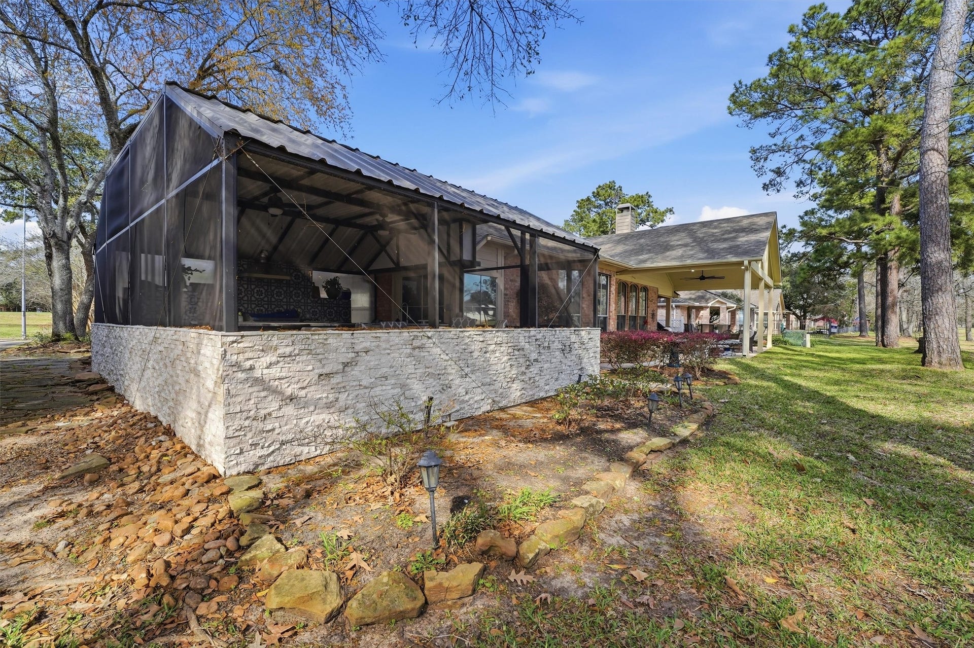 This photo showcases a charming home with a screened outdoor kitchen and dining area, perfect for relaxing or entertaining. The house is surrounded by a spacious, grassy yard with mature trees, offering a serene, natural setting.  This house is located on the golf course, hole 3.