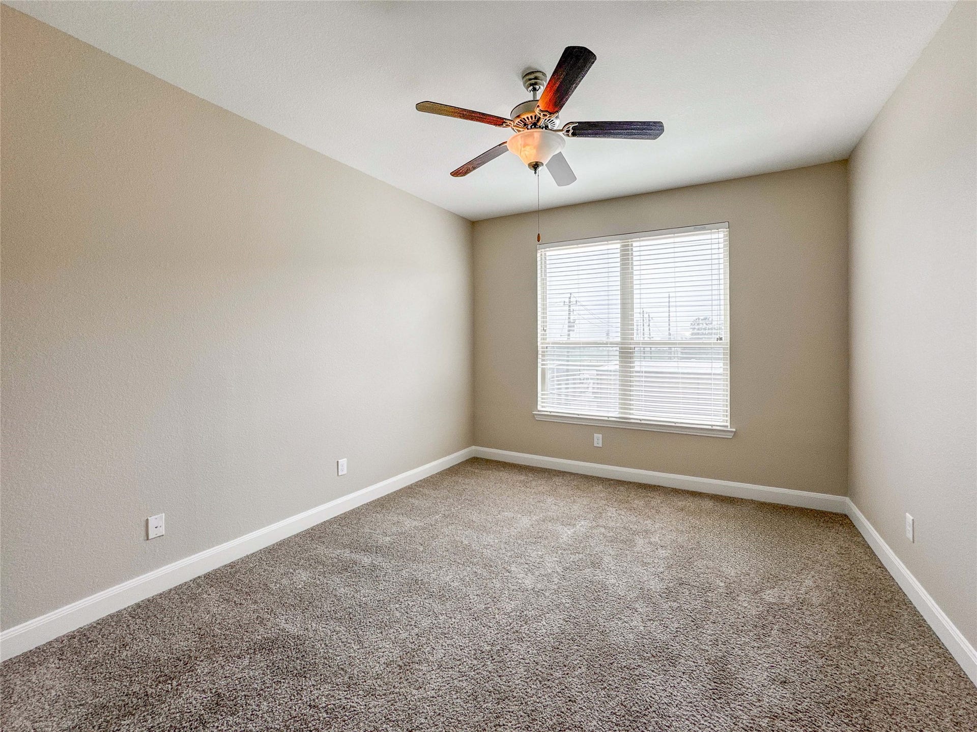 This secondary bedroom features neutral walls, a plush carpet, and a ceiling fan. It has a large window that allows natural light to fill the space, creating a bright and inviting atmosphere.